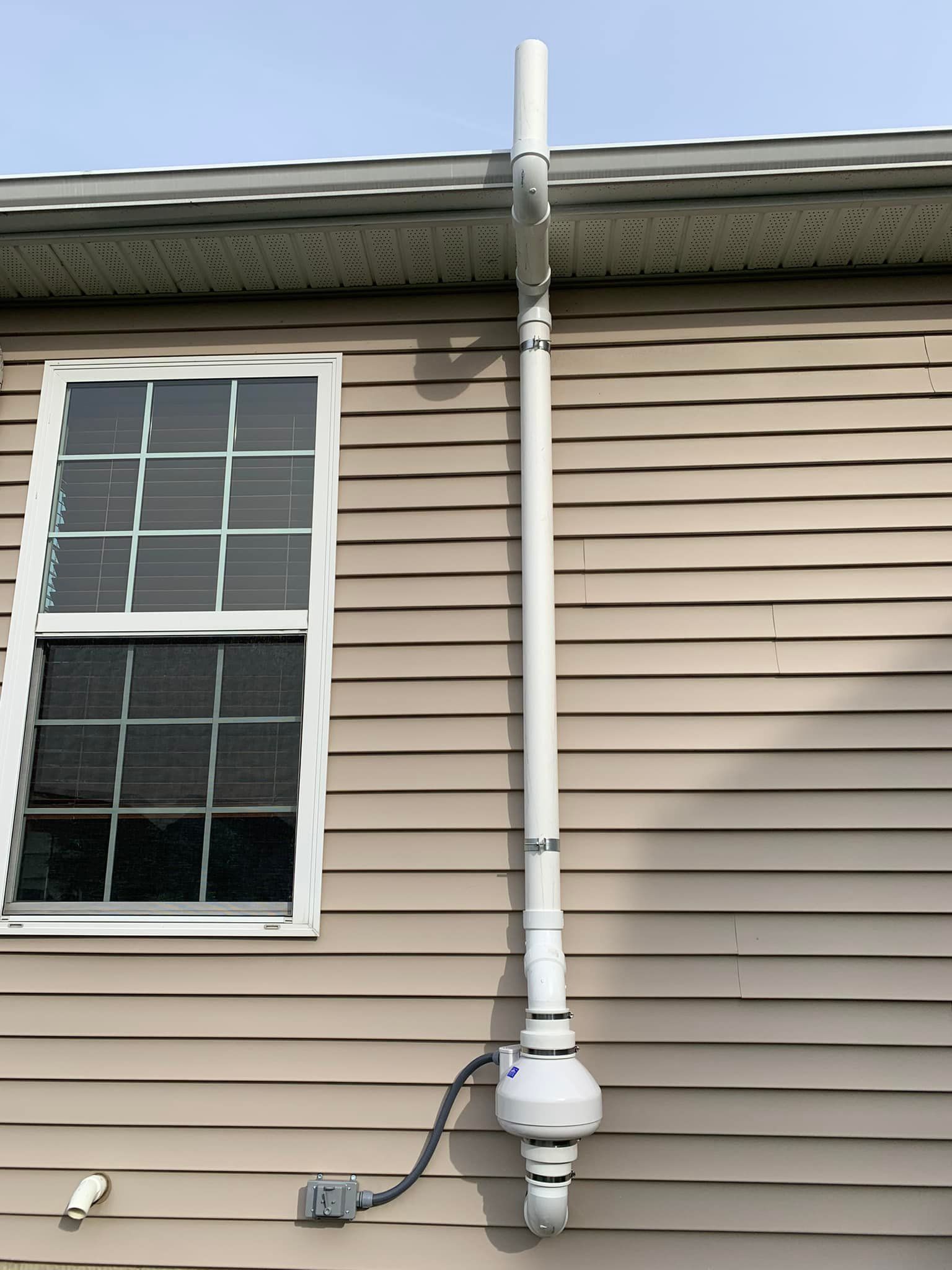A white pipe is attached to the side of a house next to a window.