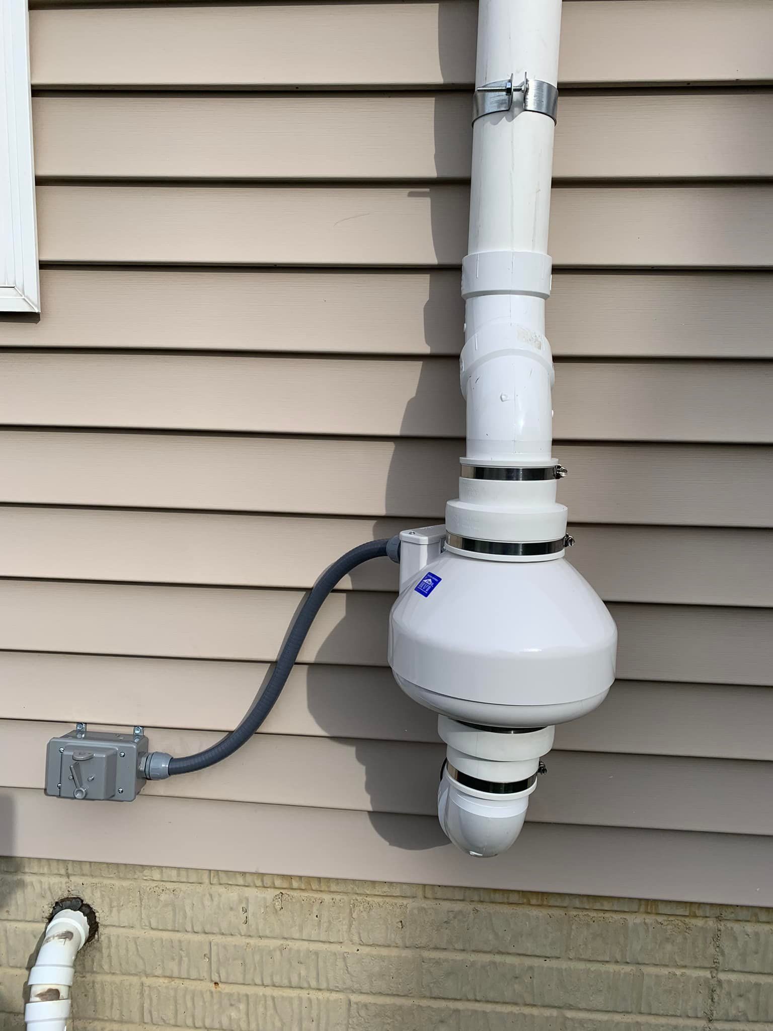 A white pipe is attached to the side of a house.