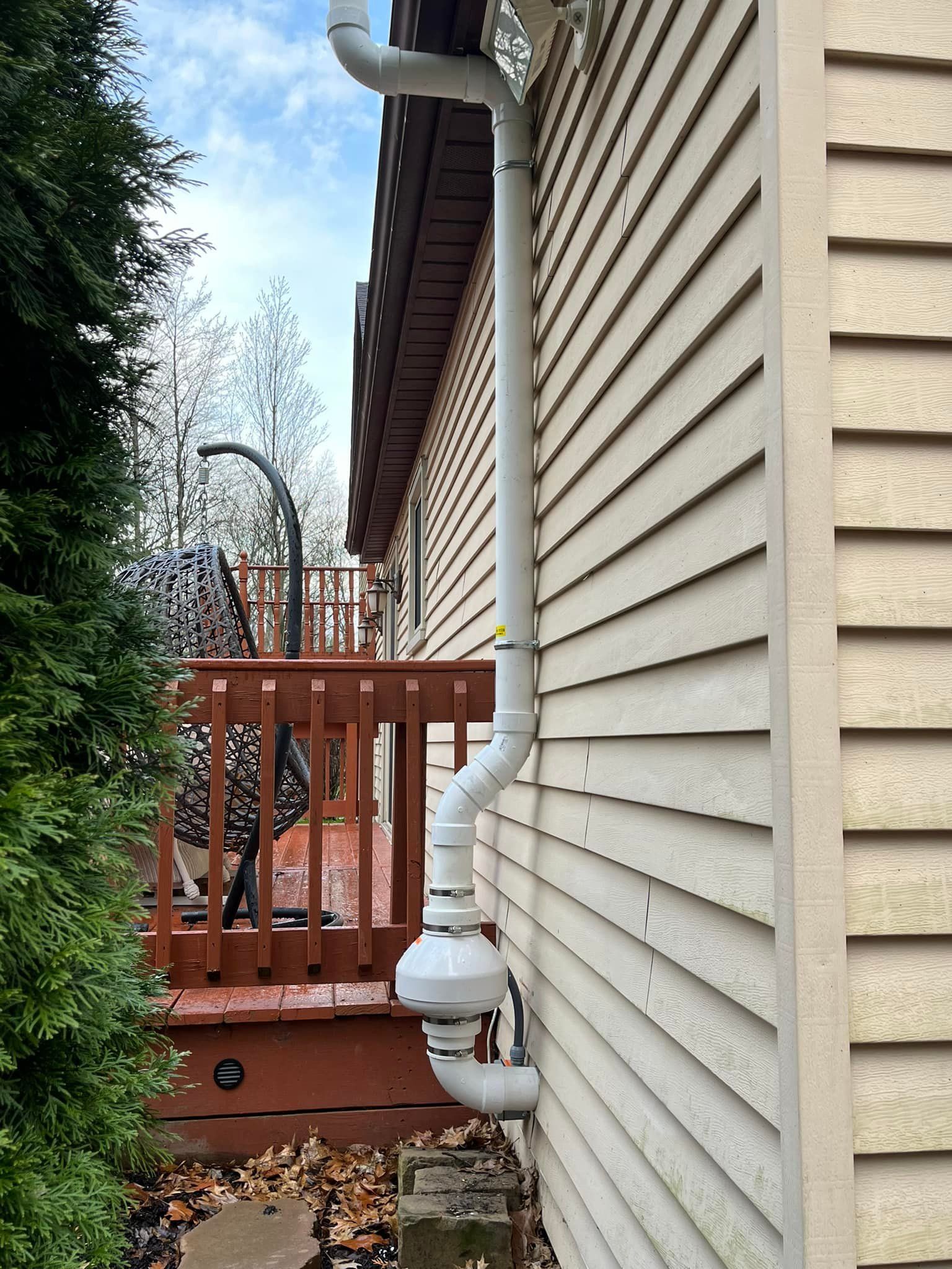 A white pipe is attached to the side of a house next to a deck.
