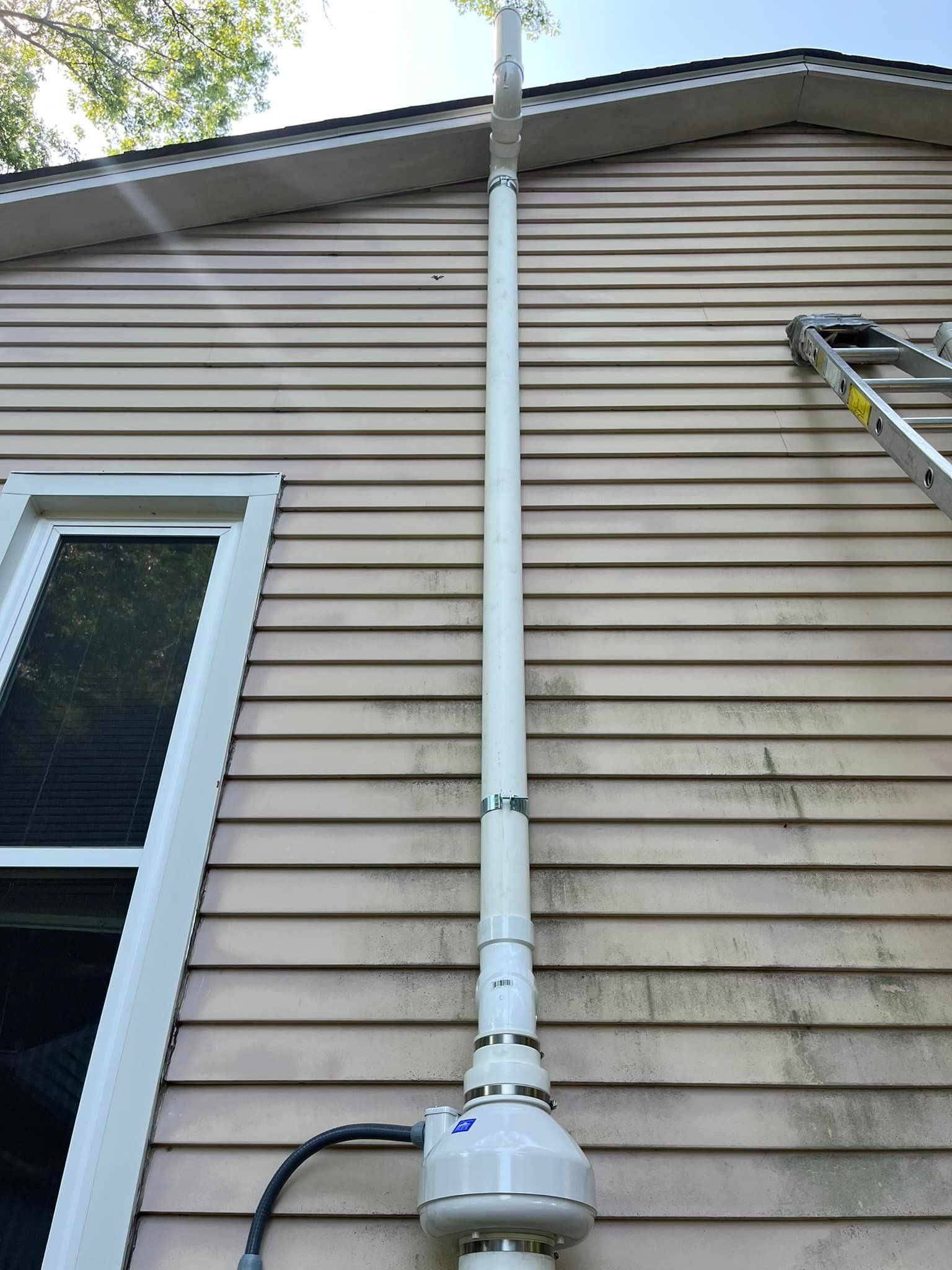 A white pipe is attached to the side of a house.