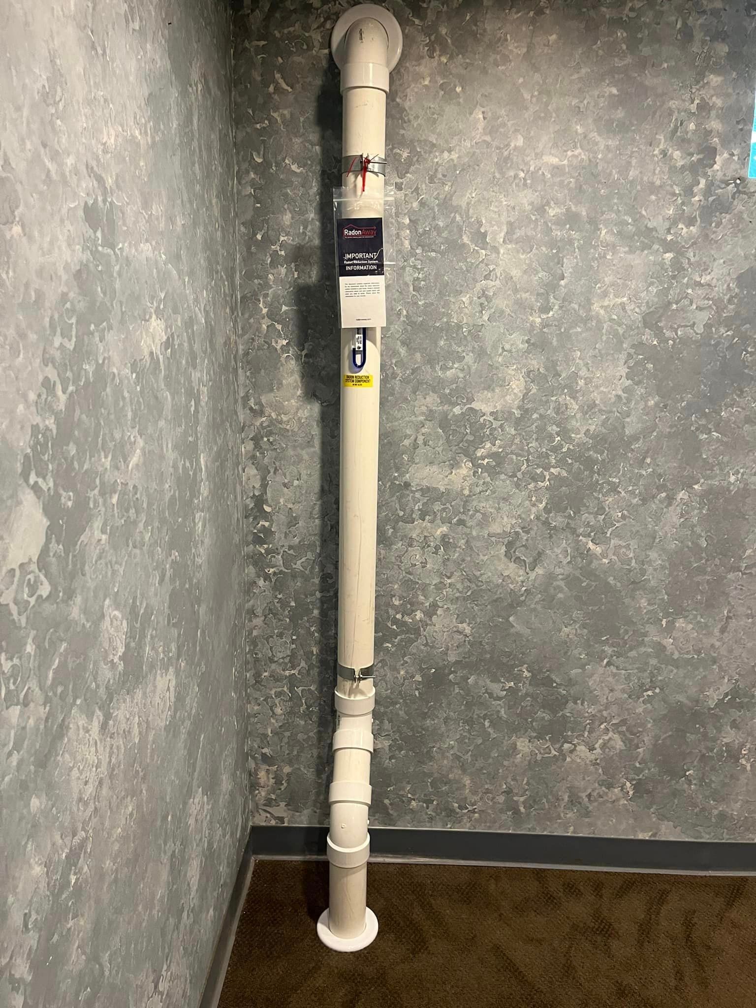 A white pipe is sitting in a corner of a room next to a wall.