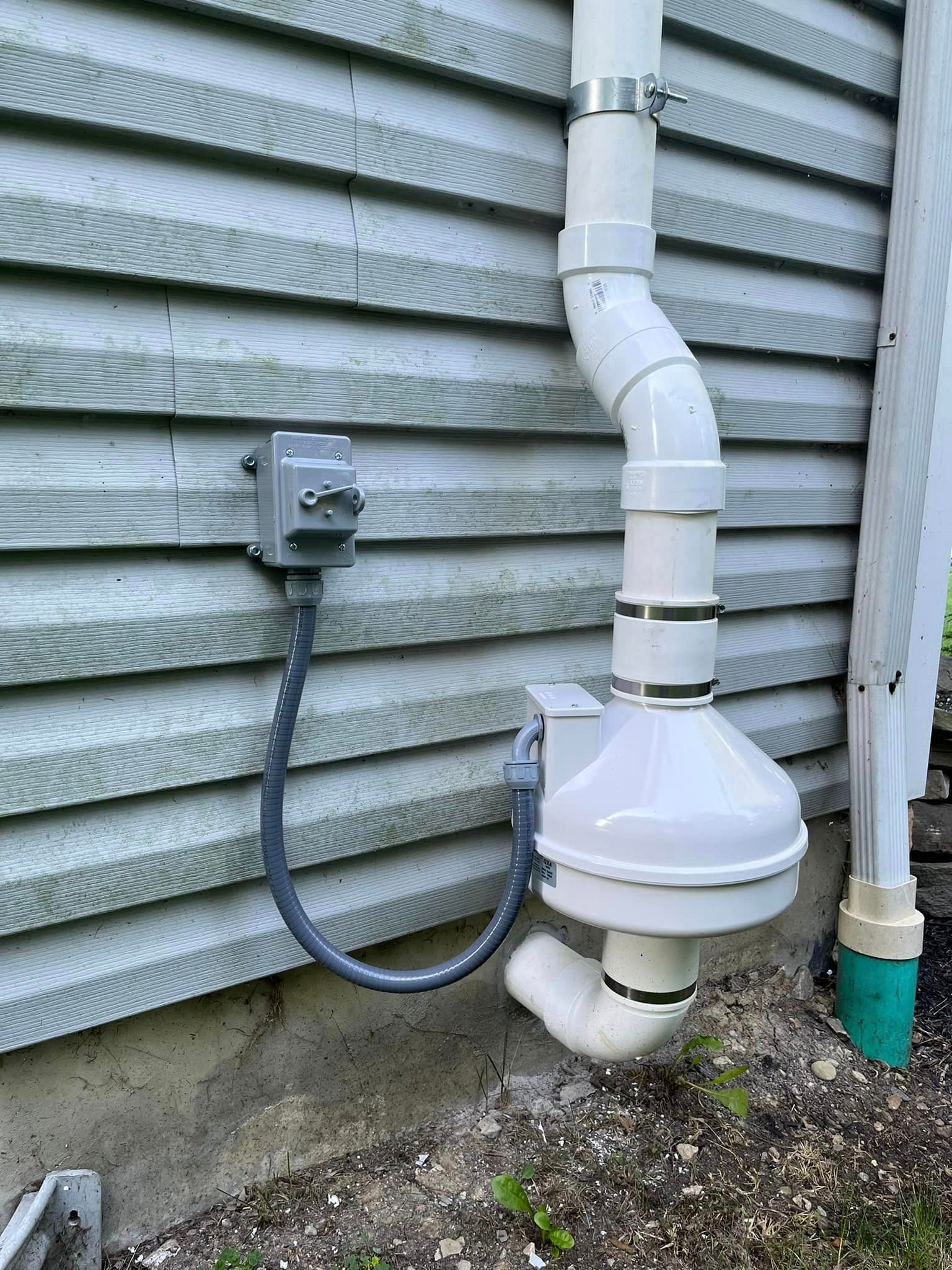 A white pipe is attached to the side of a house.