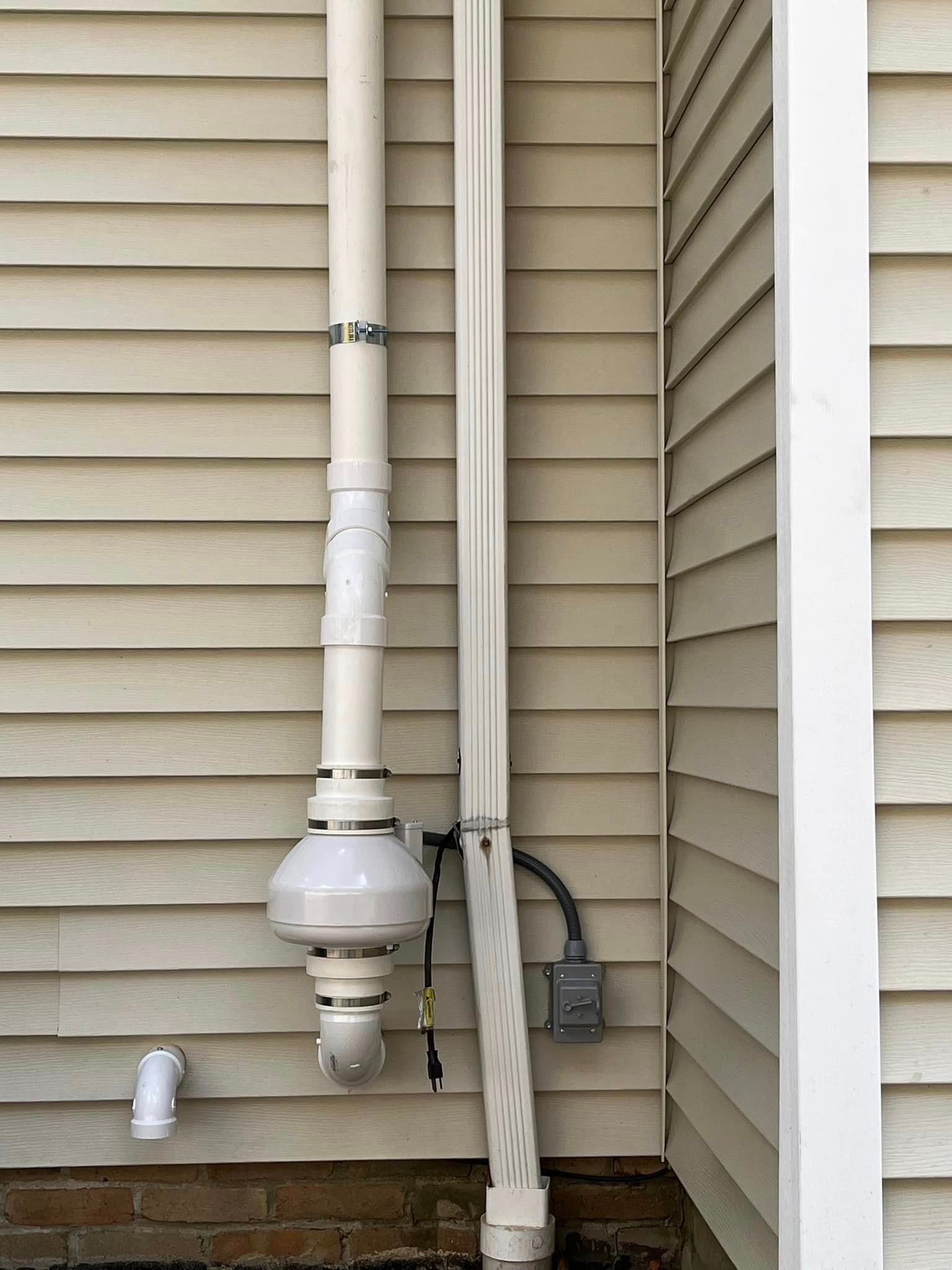 A white pipe is attached to the side of a house.