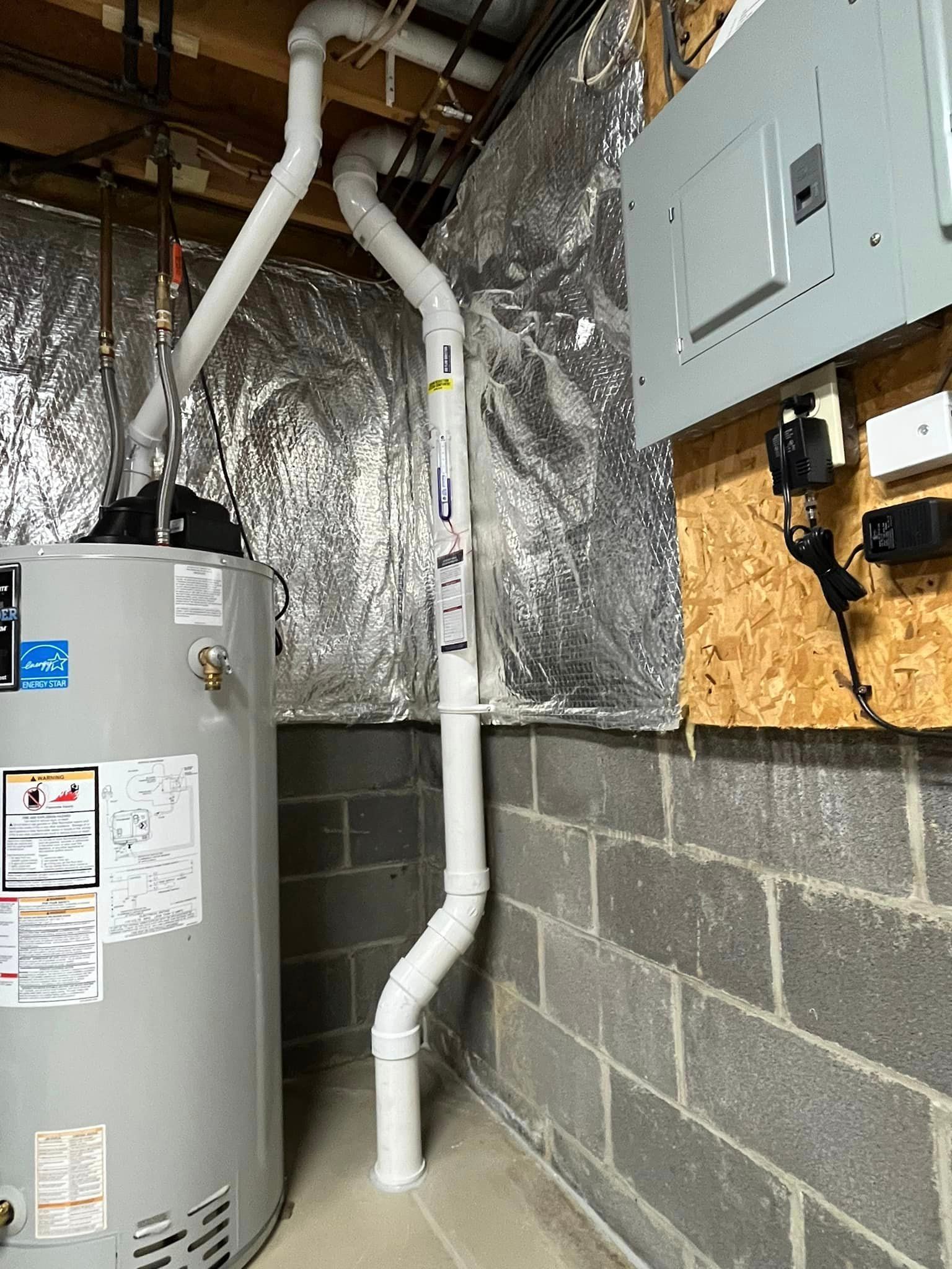 A water heater is sitting in a basement next to a brick wall.