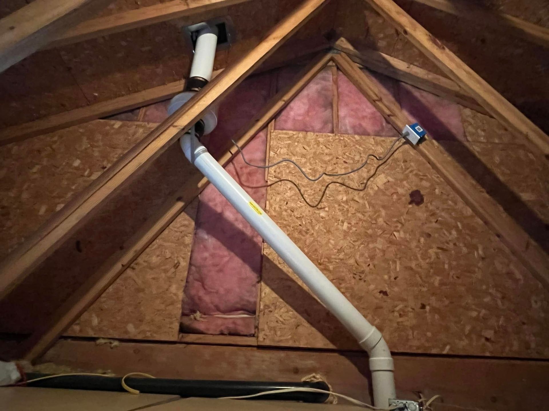 A white pipe is hanging from the ceiling of an attic.