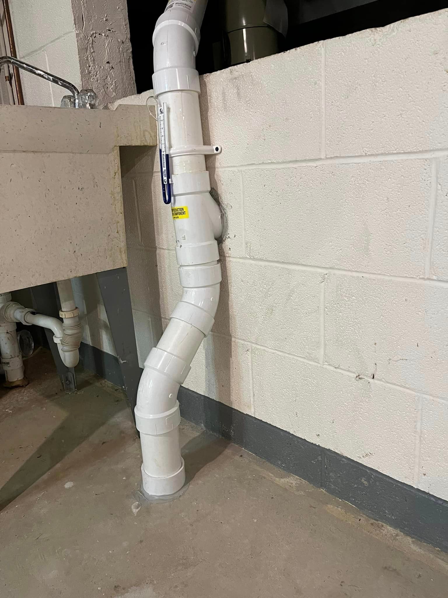 A white pipe is sitting next to a brick wall.