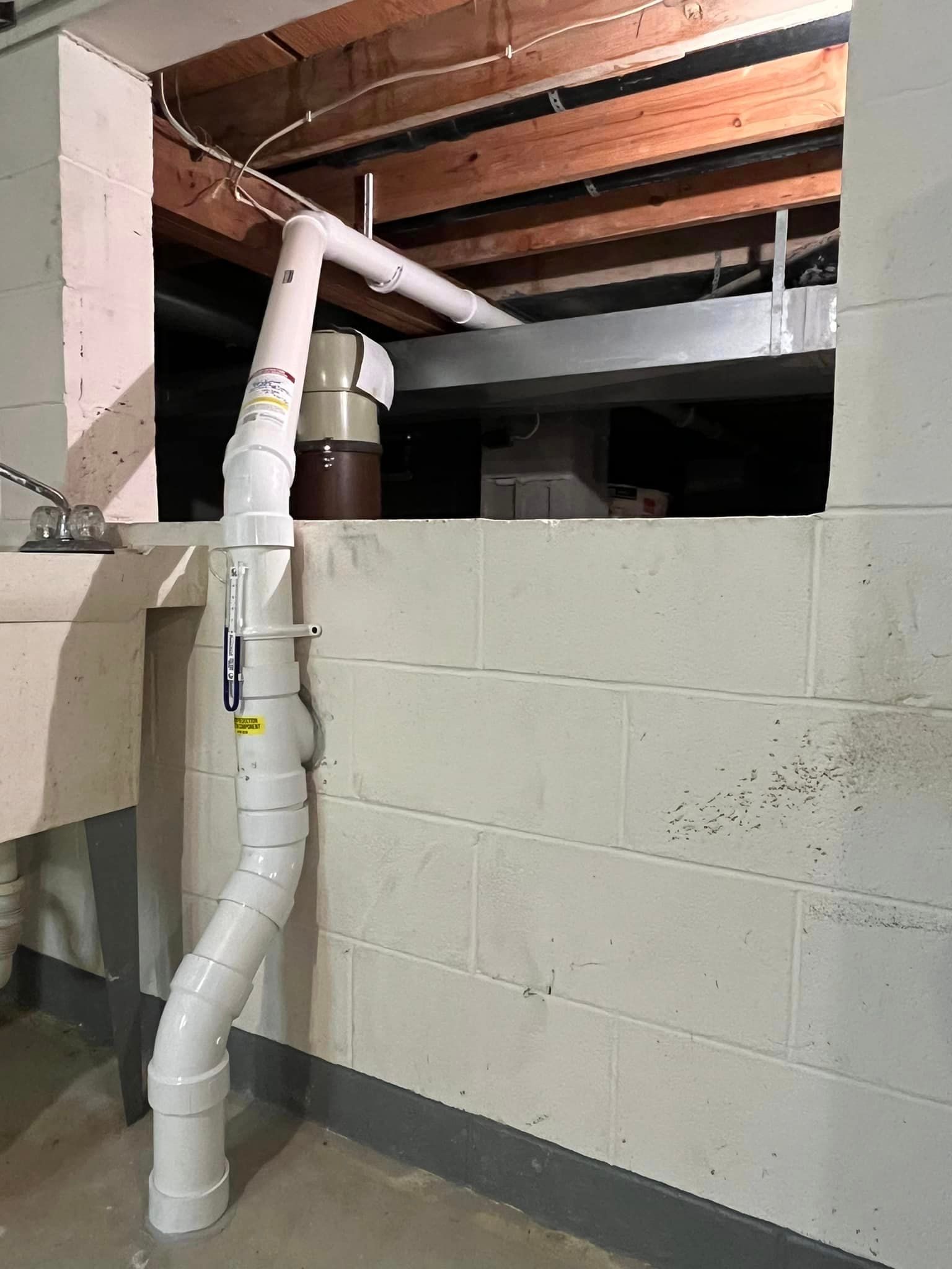 A white pipe is hanging from the ceiling in a basement next to a sink.