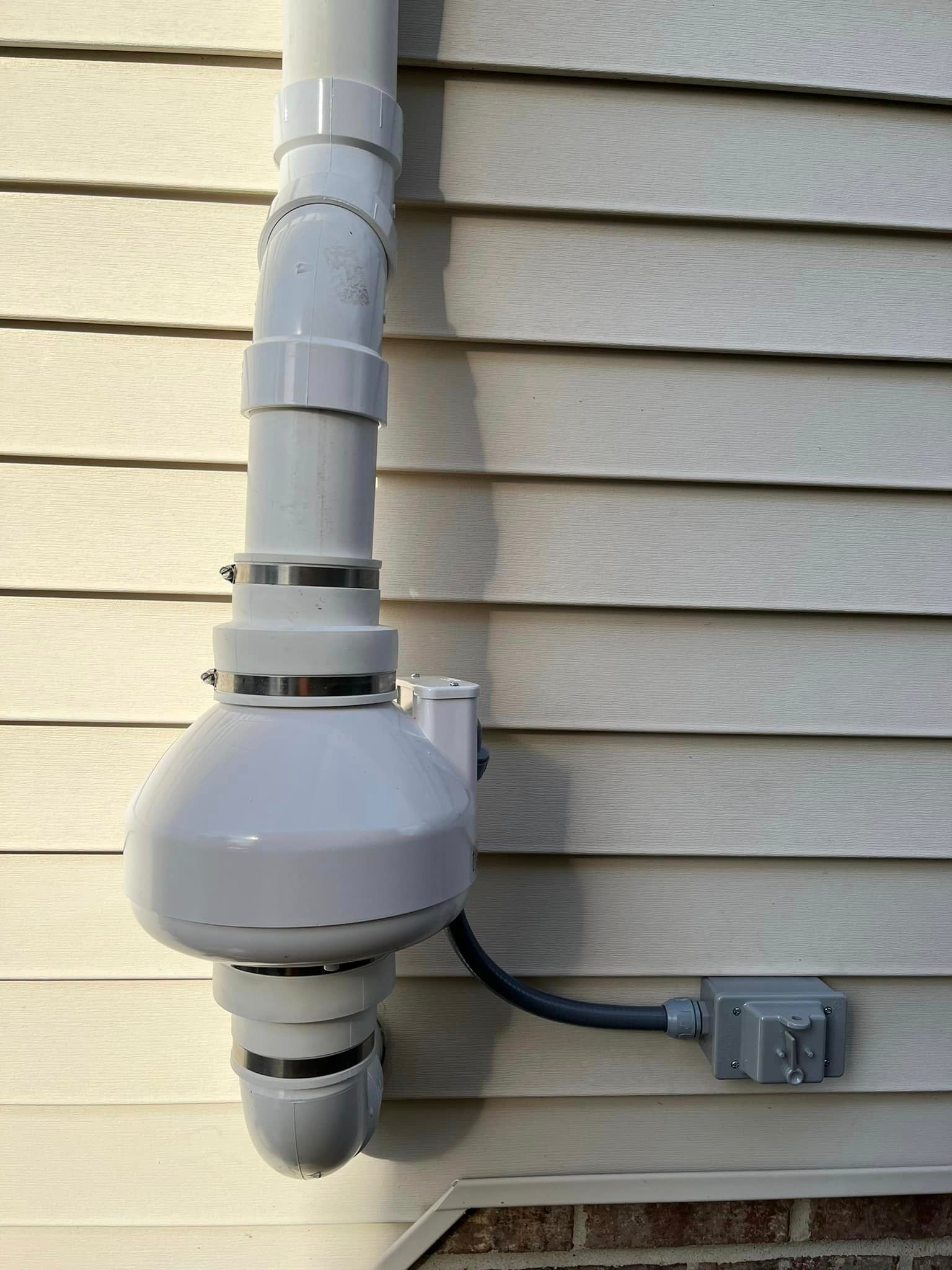 A white pipe is attached to the side of a house.