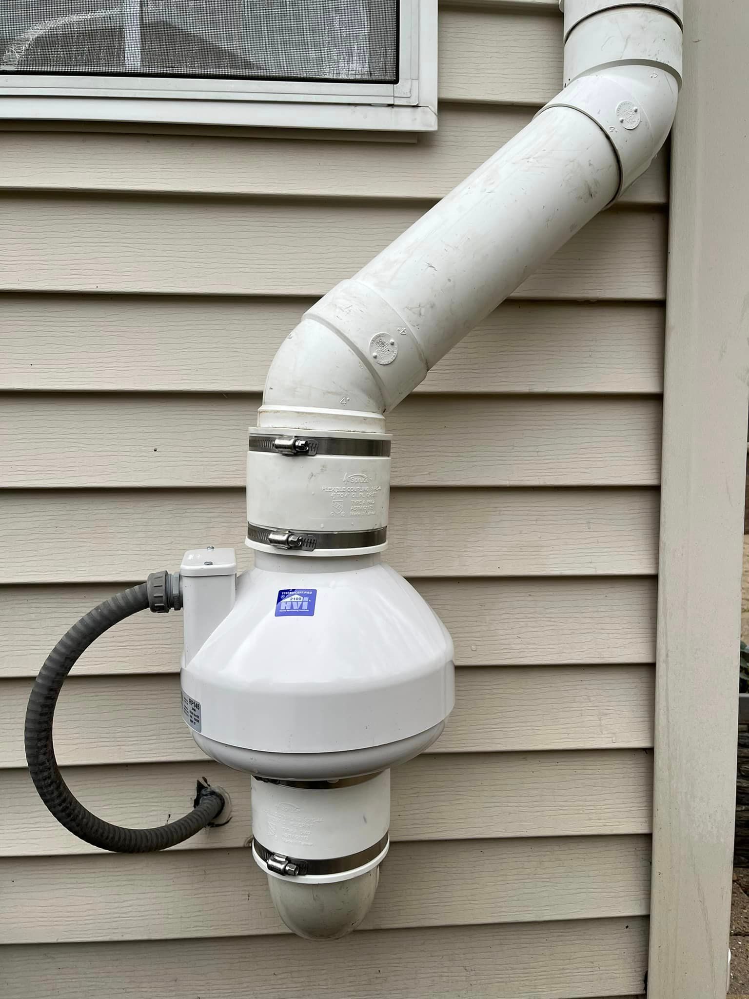 A white pipe is attached to the side of a house.