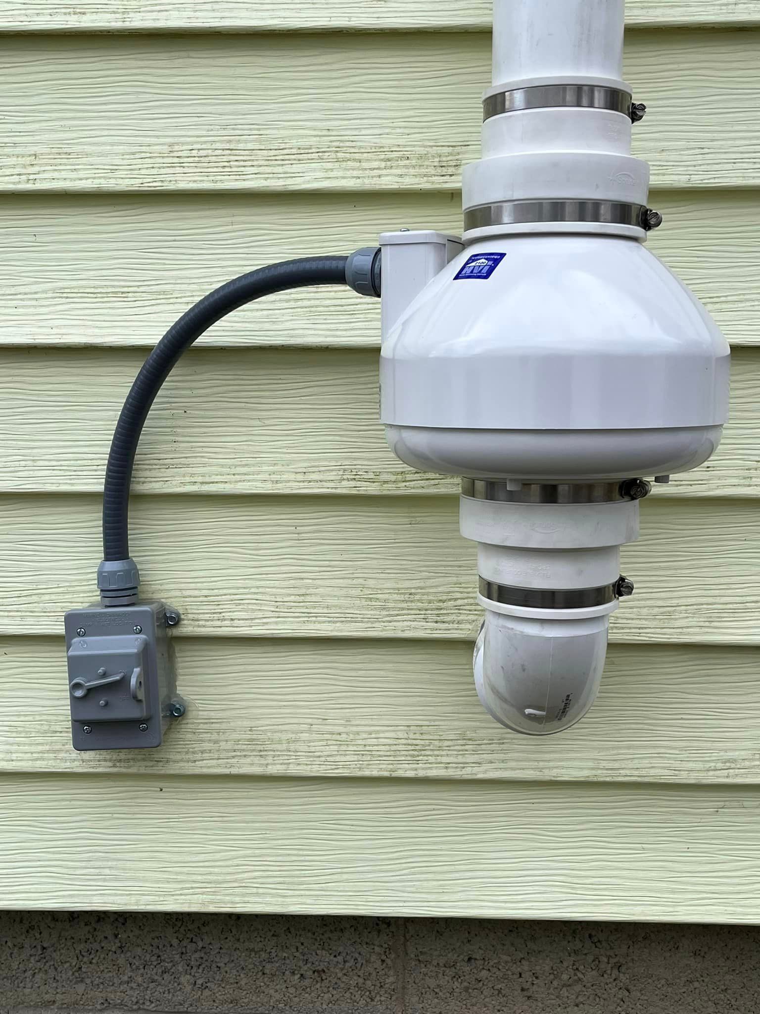 A white exhaust fan is attached to the side of a house.