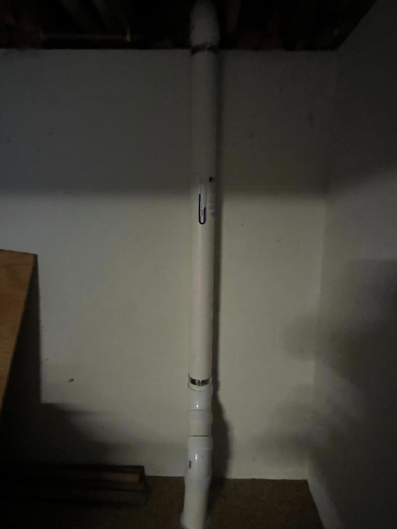 A white pipe is sitting in a dark room next to a wall.