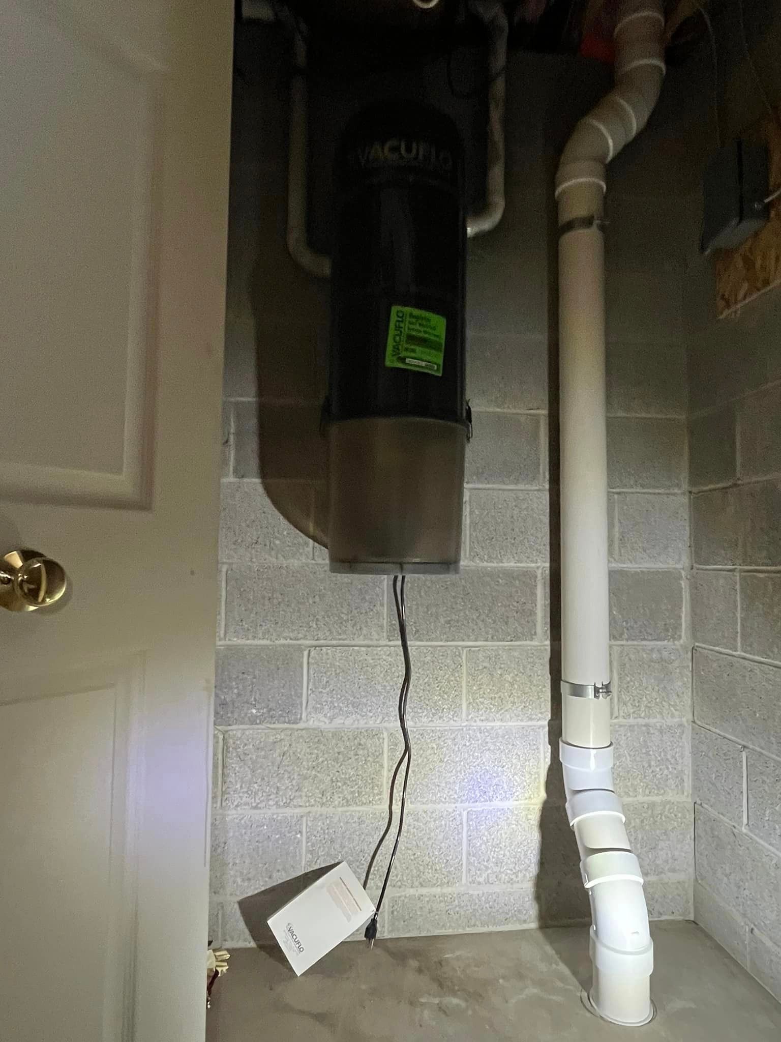 A vacuum cleaner is hanging from the ceiling in a basement next to a pipe.