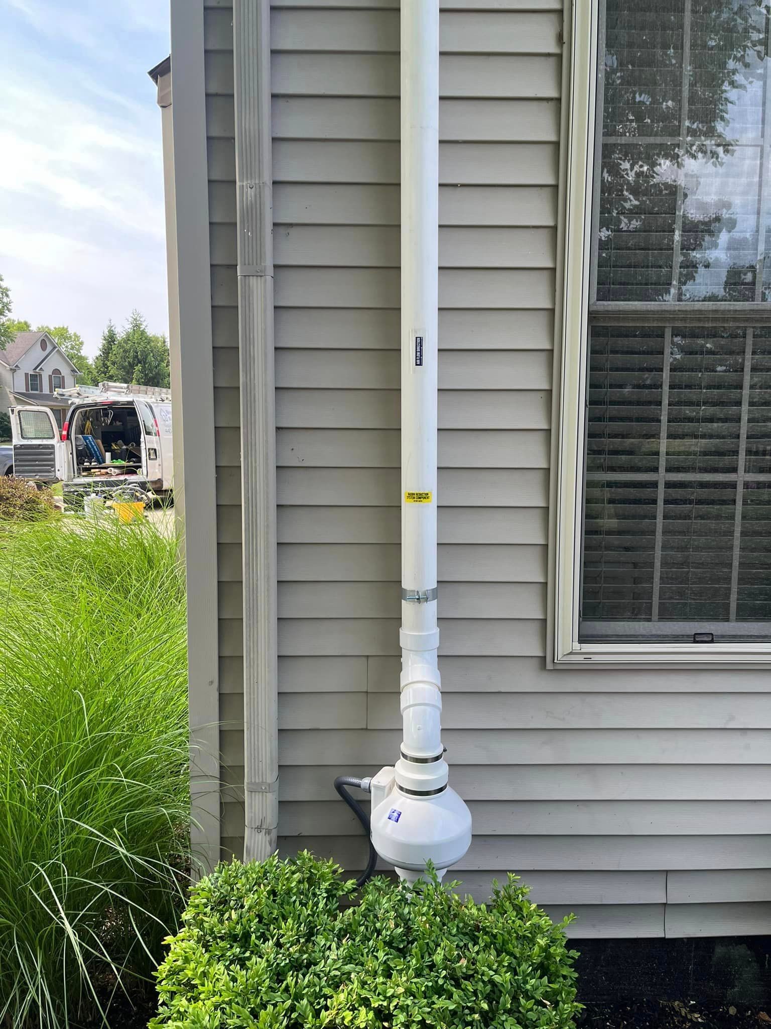 A white pipe is attached to the side of a house next to a window.