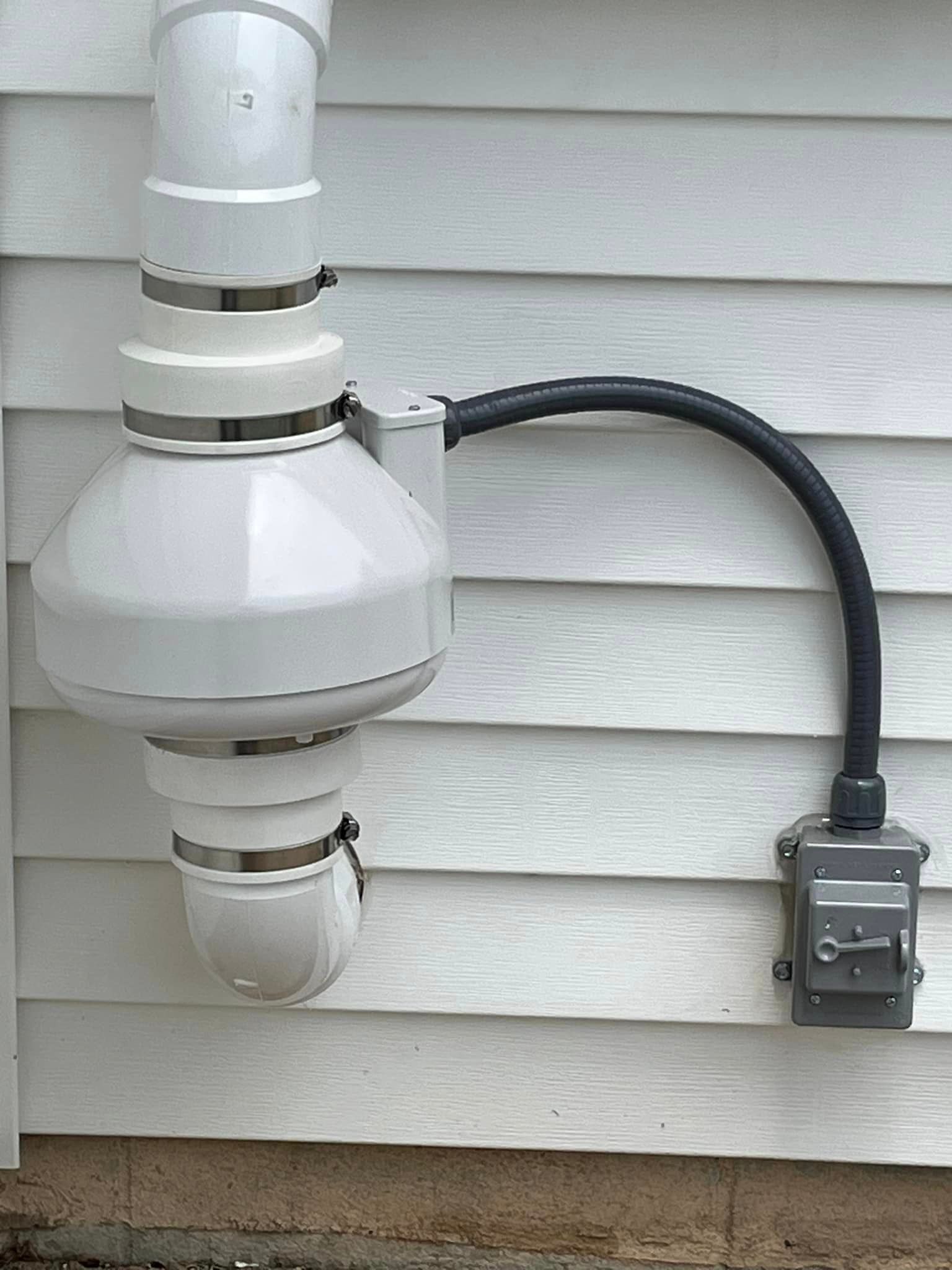 A white pipe is attached to the side of a house.