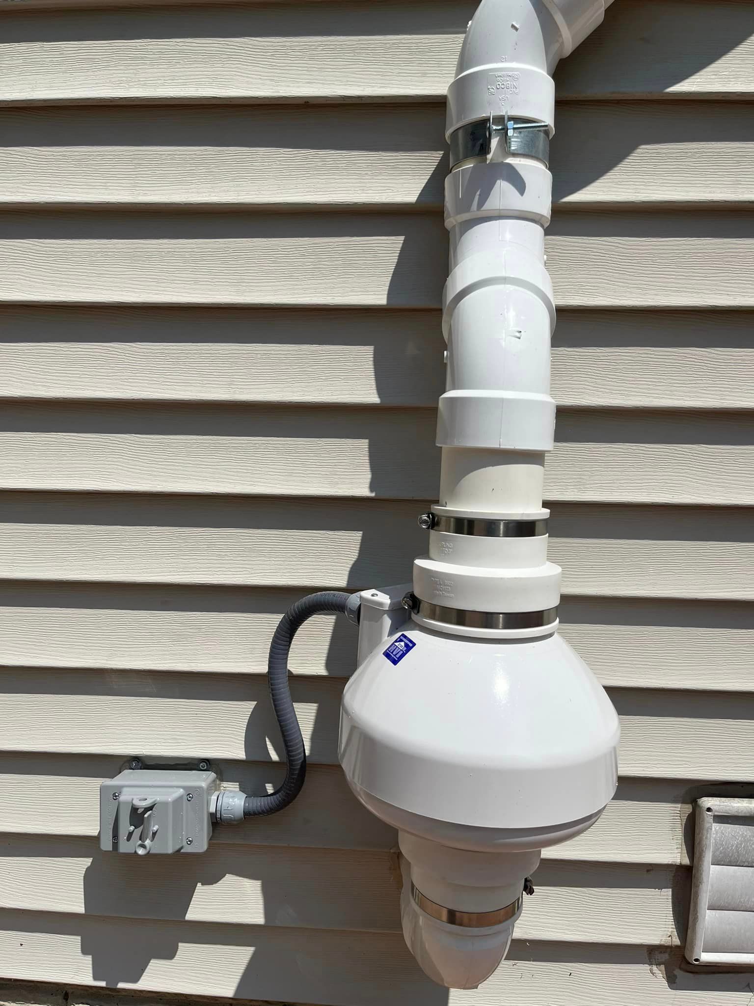 A white pipe is attached to the side of a house.