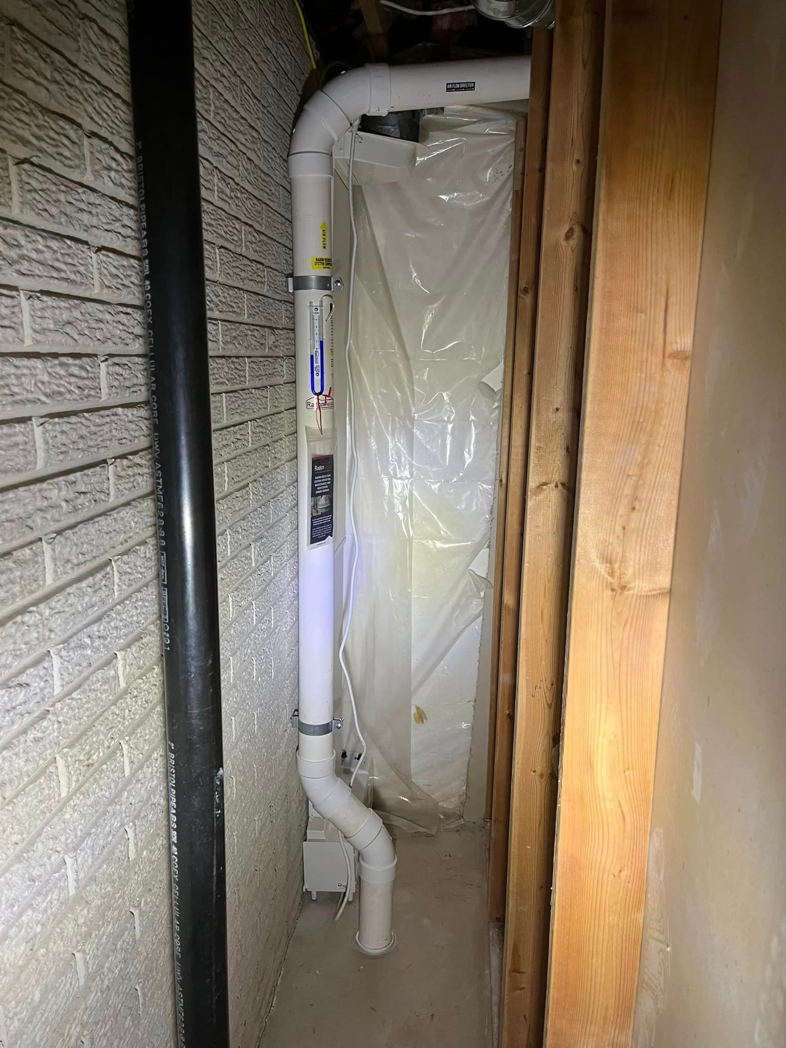 A white pipe is hanging from a brick wall in a basement.