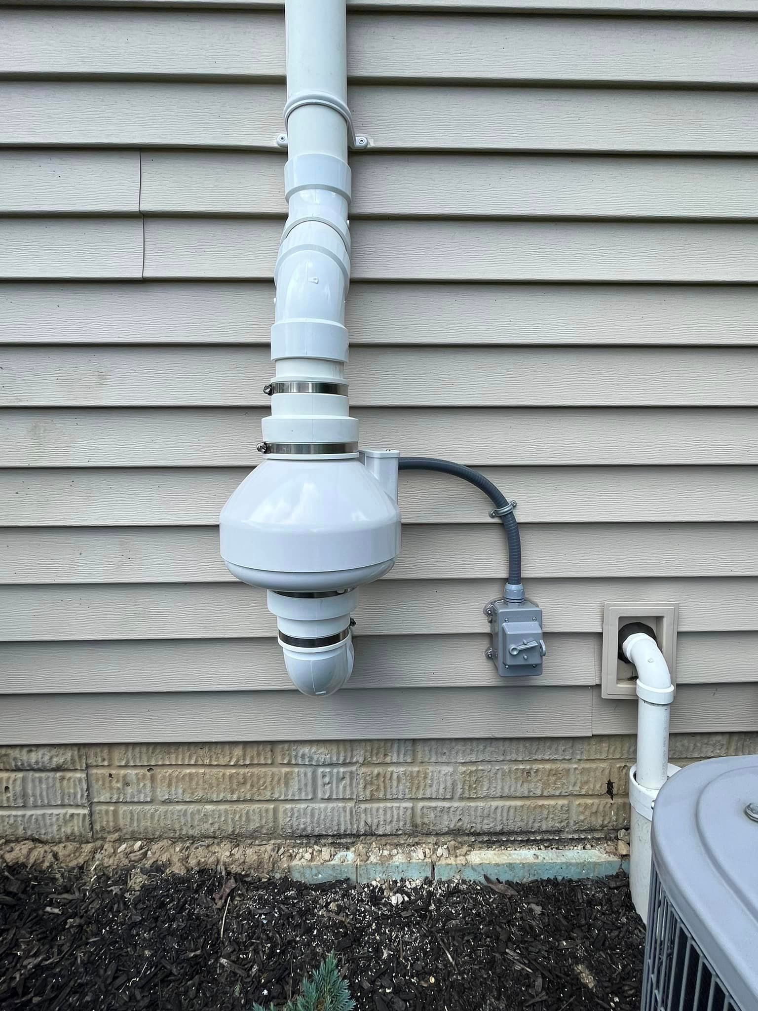 A white pipe is attached to the side of a house next to an air conditioner.