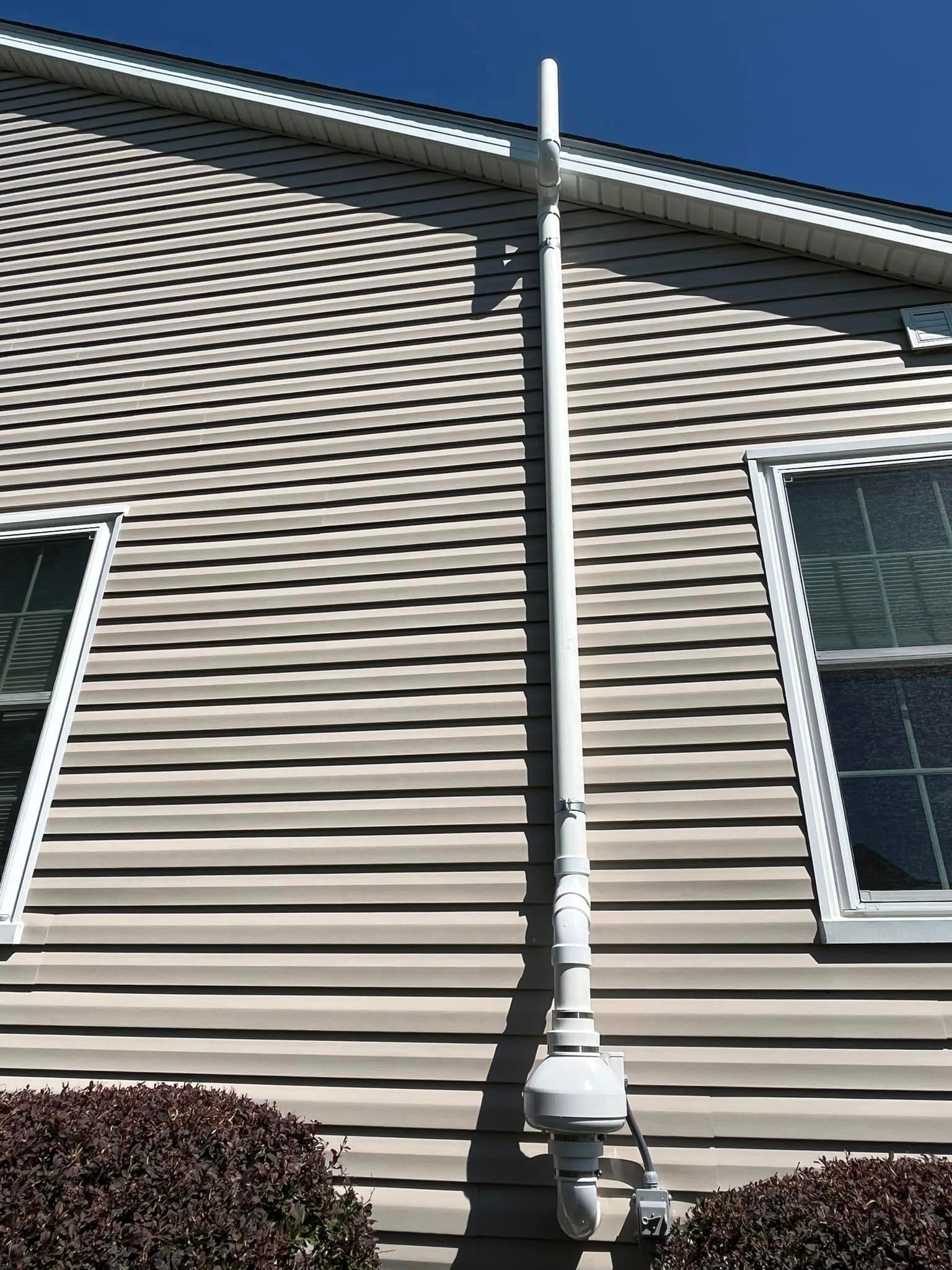 A white pipe is attached to the side of a house.