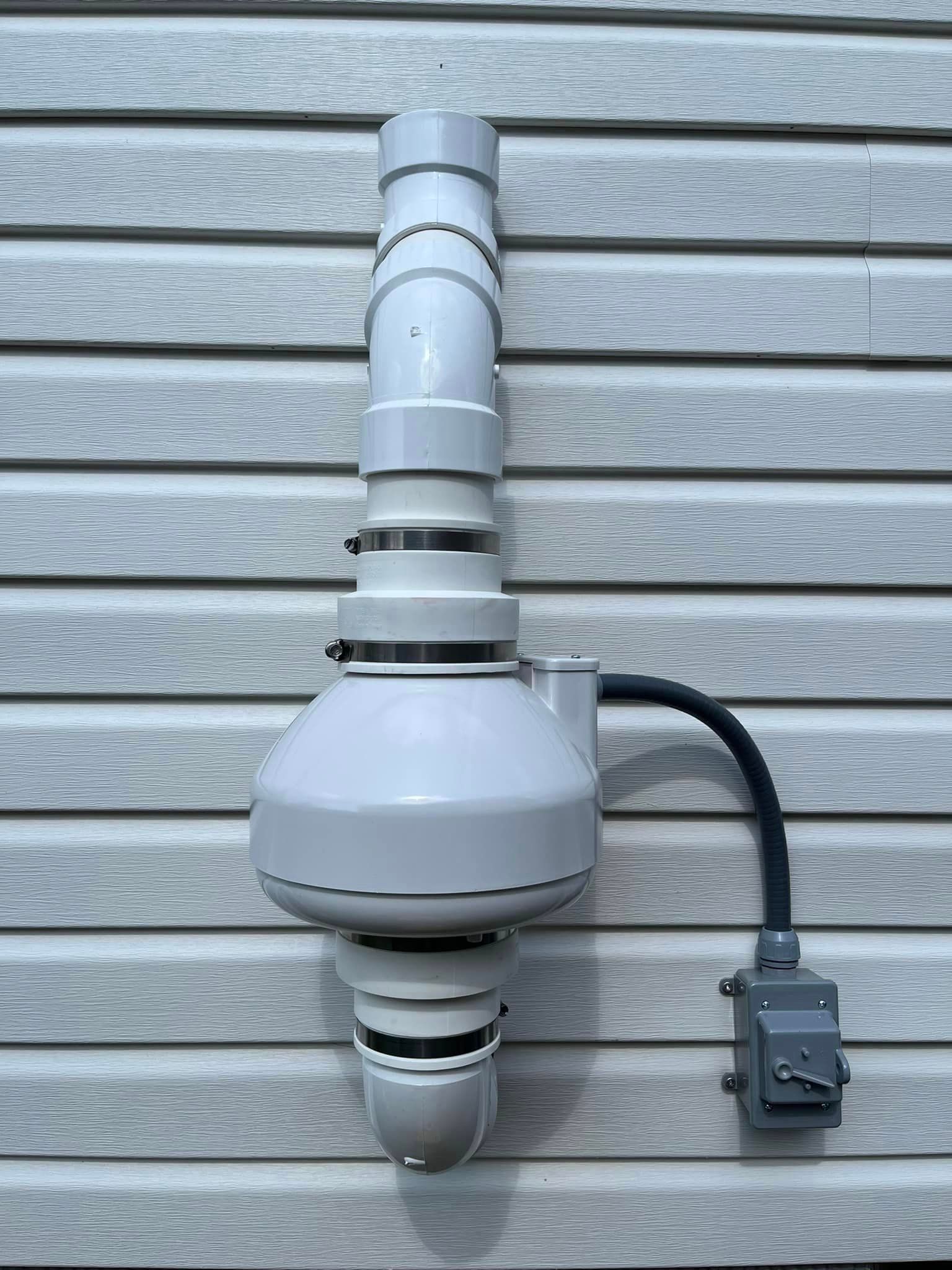 A white pipe is attached to the side of a house.