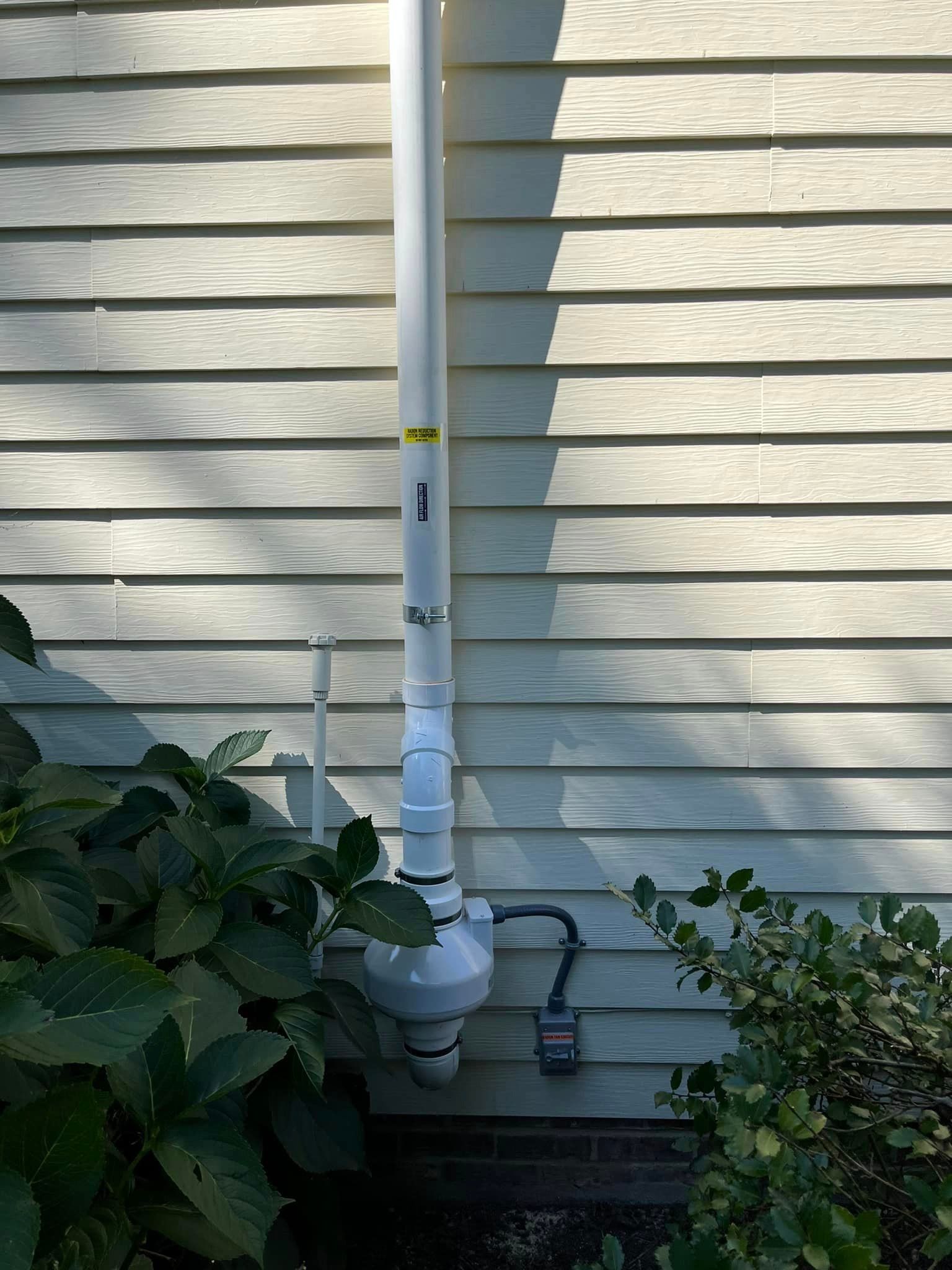 A white pipe is attached to the side of a house.