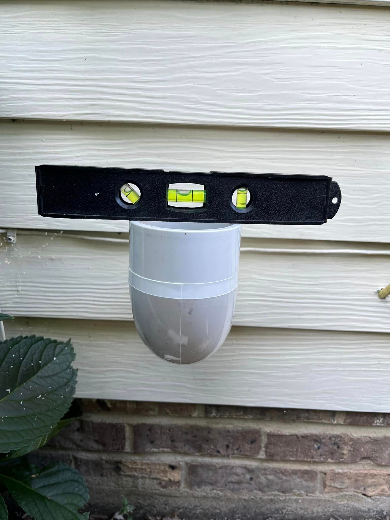 A level is attached to a pipe on the side of a house.