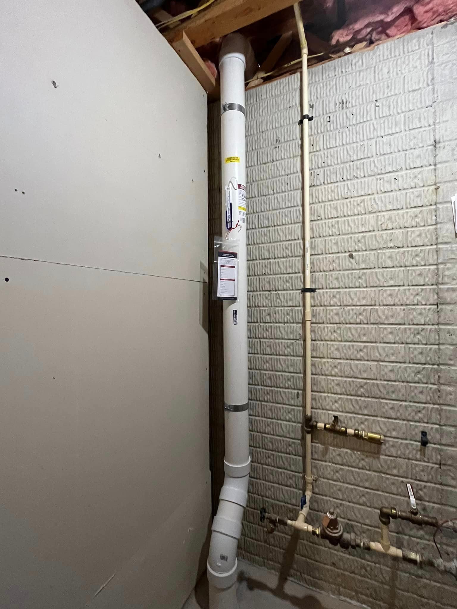 A white pipe is hanging from the ceiling in a basement next to a brick wall.