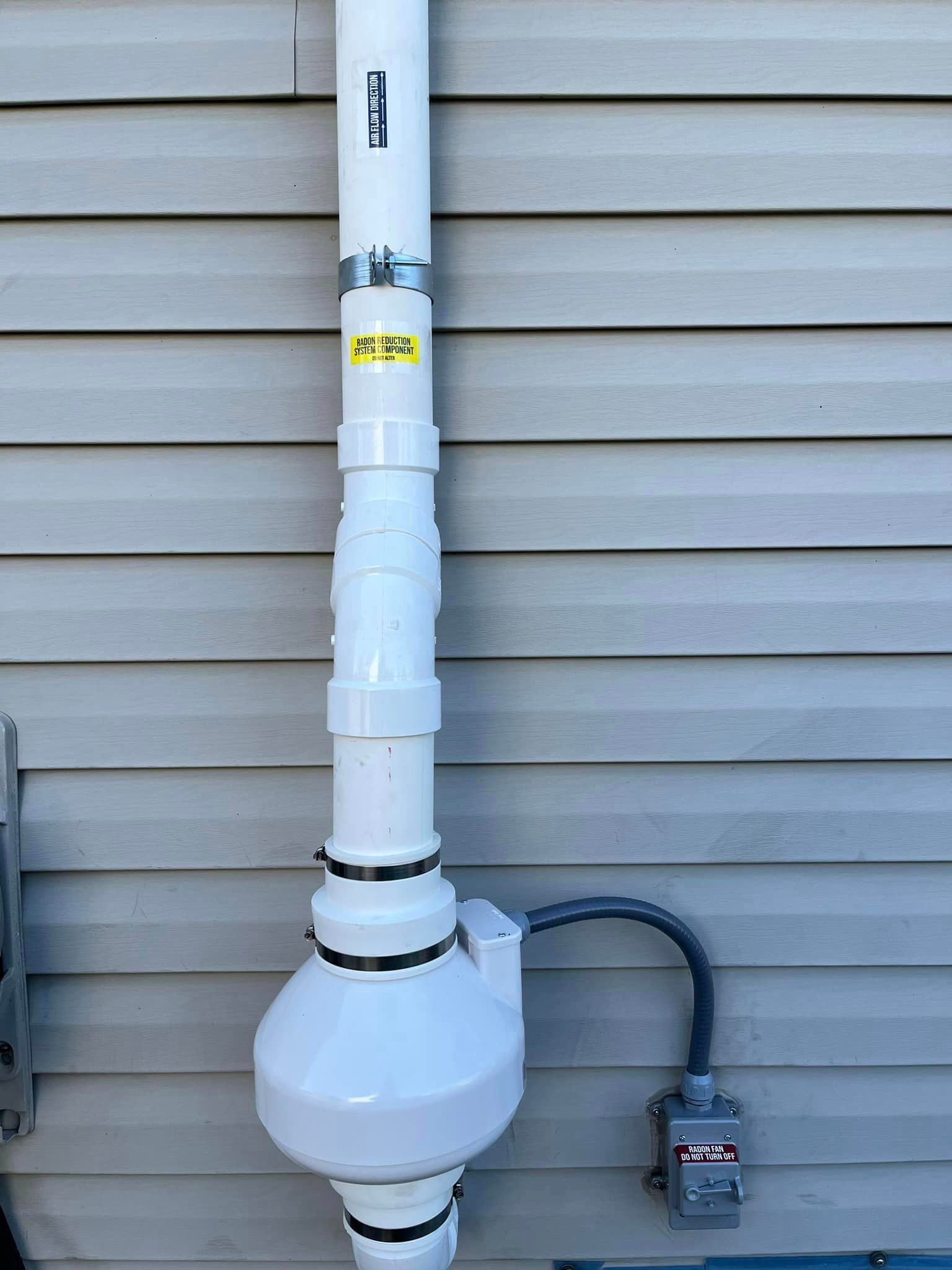 A white pipe is attached to the side of a house.