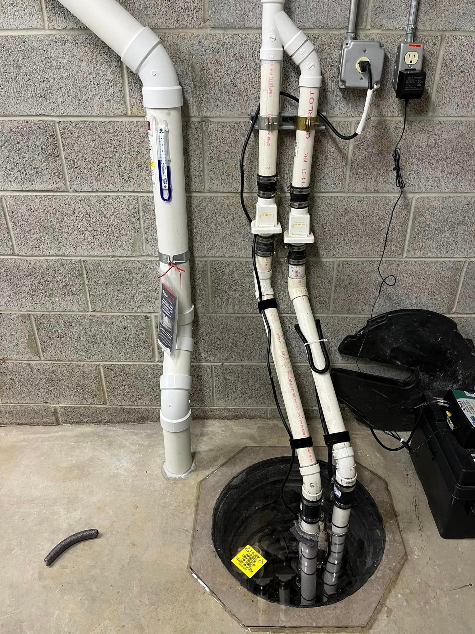 A close up of a sump pump in a basement next to a brick wall.