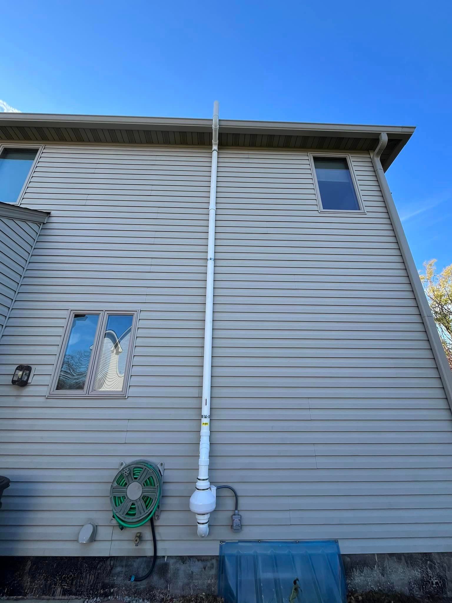 A white pipe is hanging from the side of a house.
