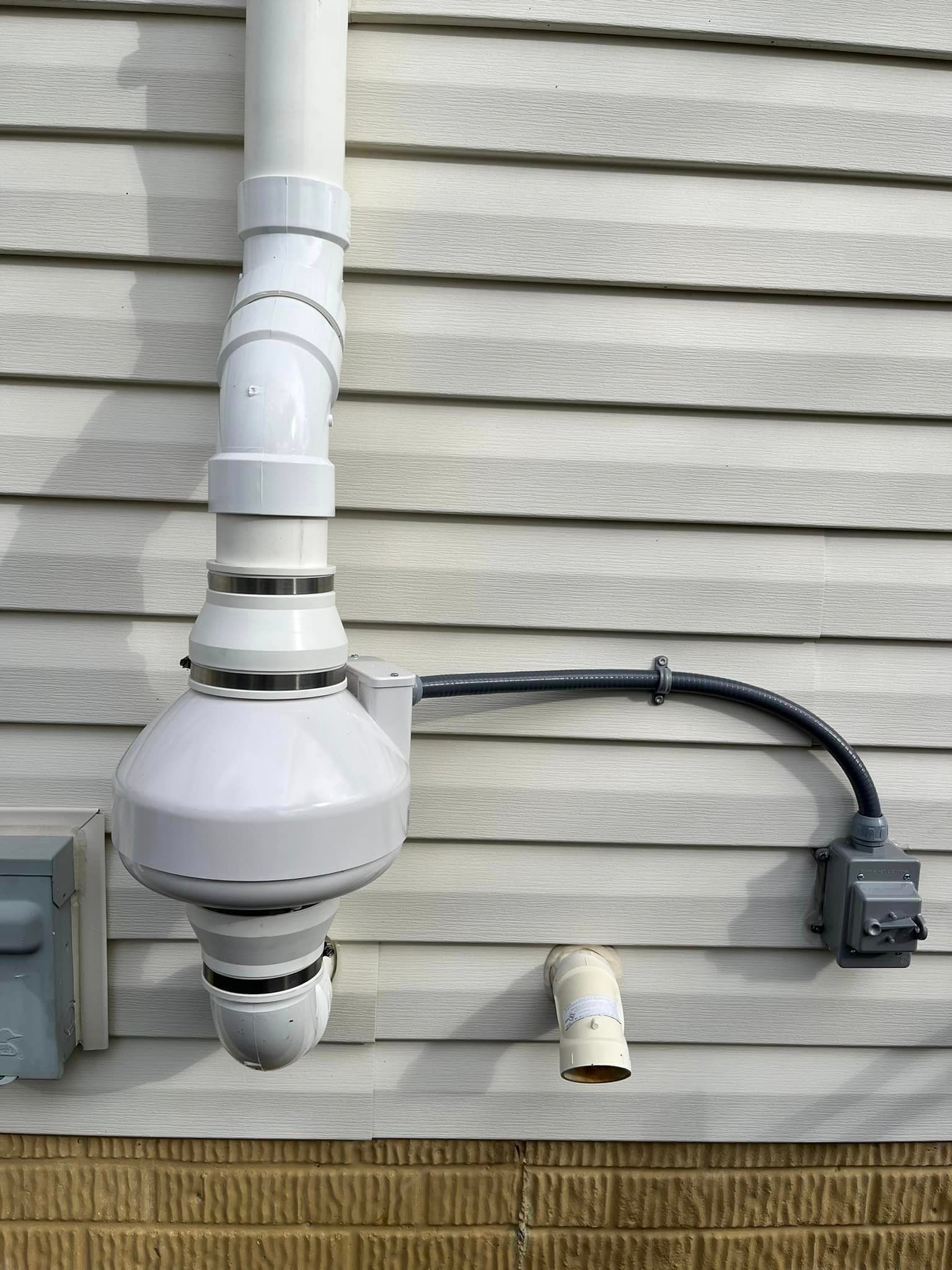 A white pipe is attached to the side of a house.