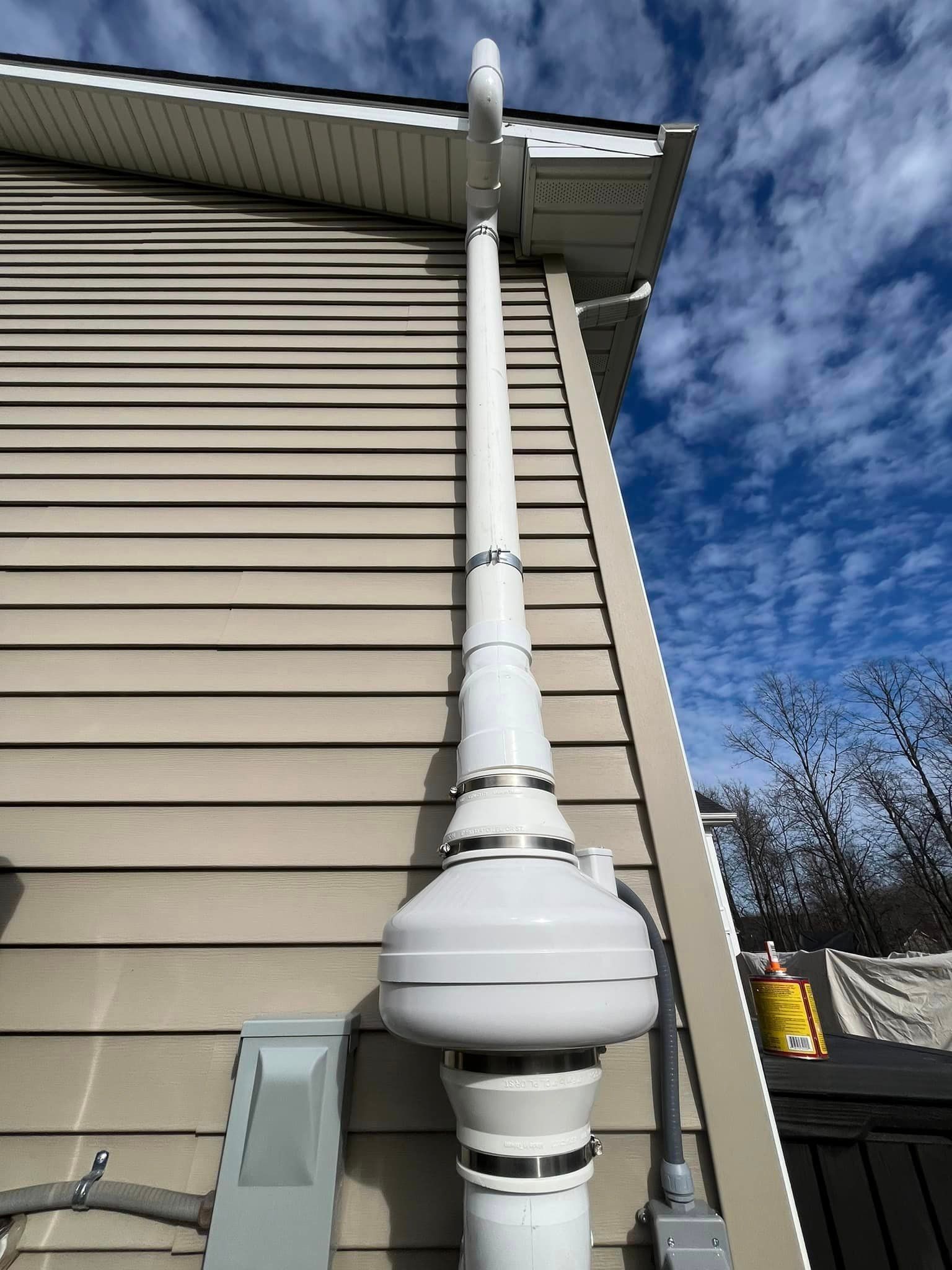 A white pipe is attached to the side of a house.