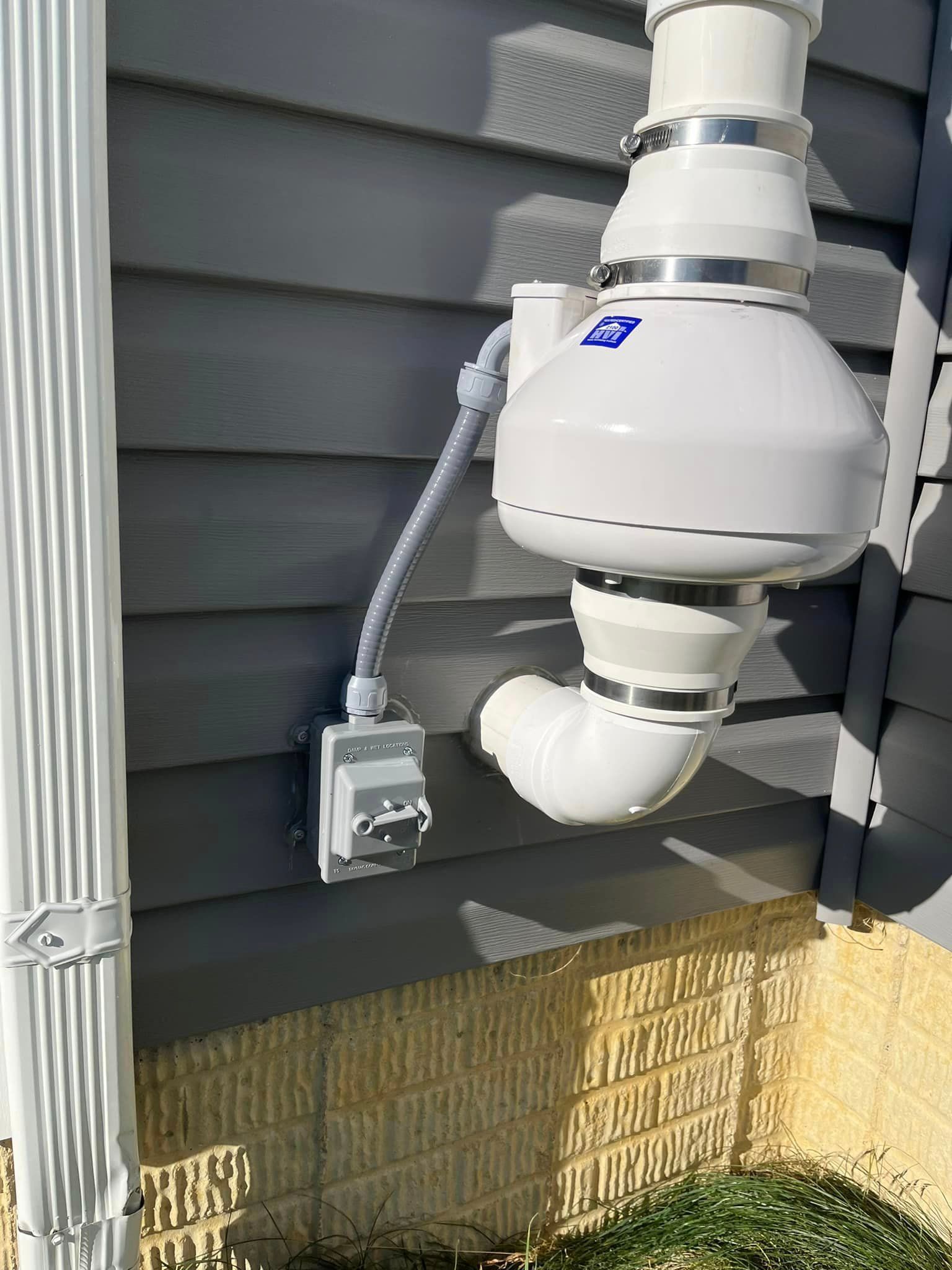 A white pipe is attached to the side of a house.