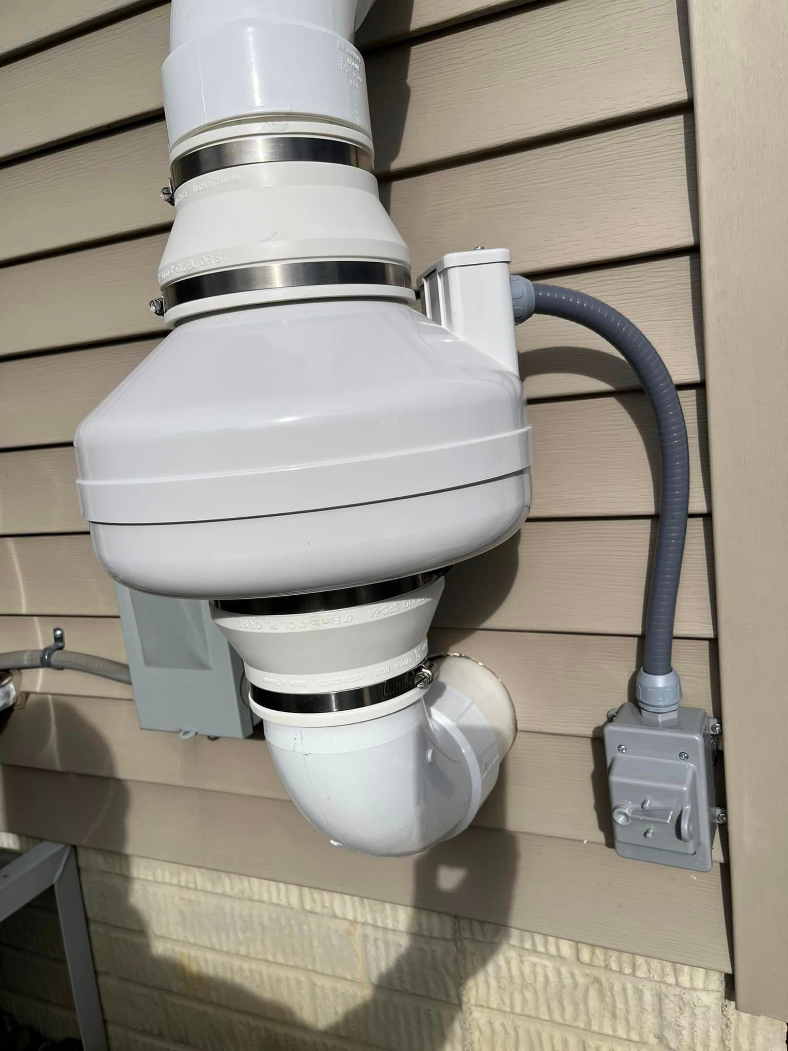 A white exhaust fan is attached to the side of a house.