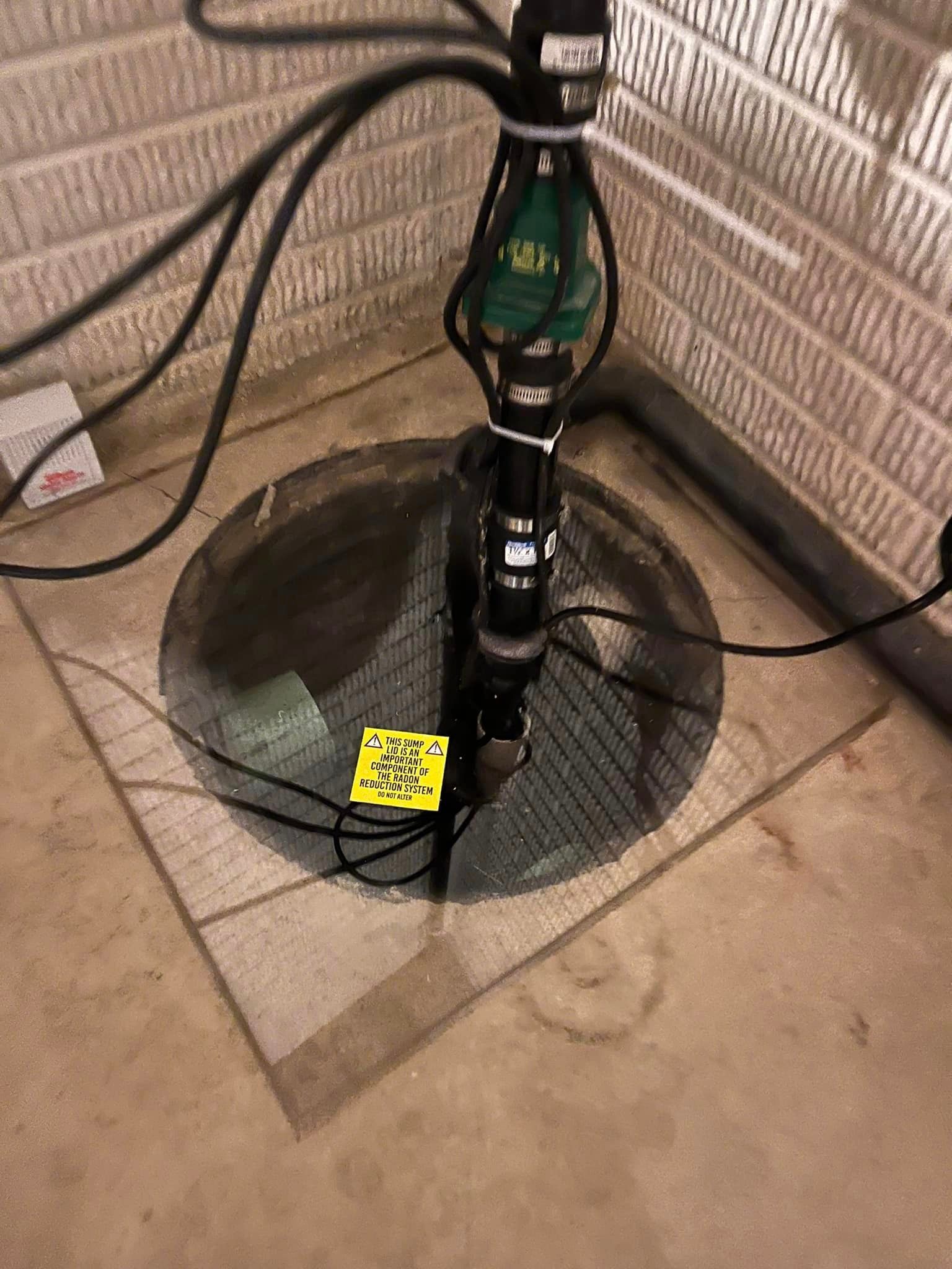 A sump pump is sitting in a basement next to a brick wall.