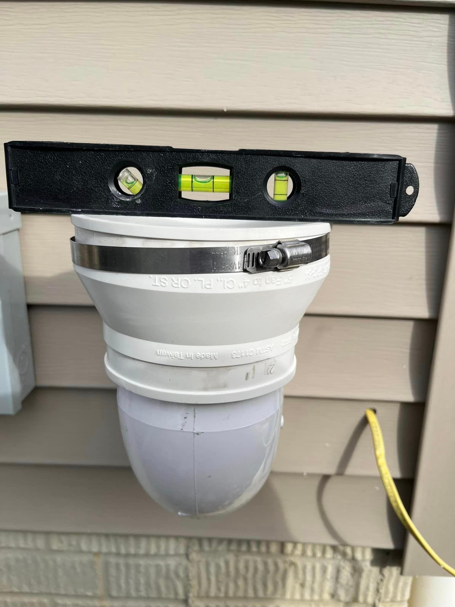 A level is attached to a pipe on the side of a house.