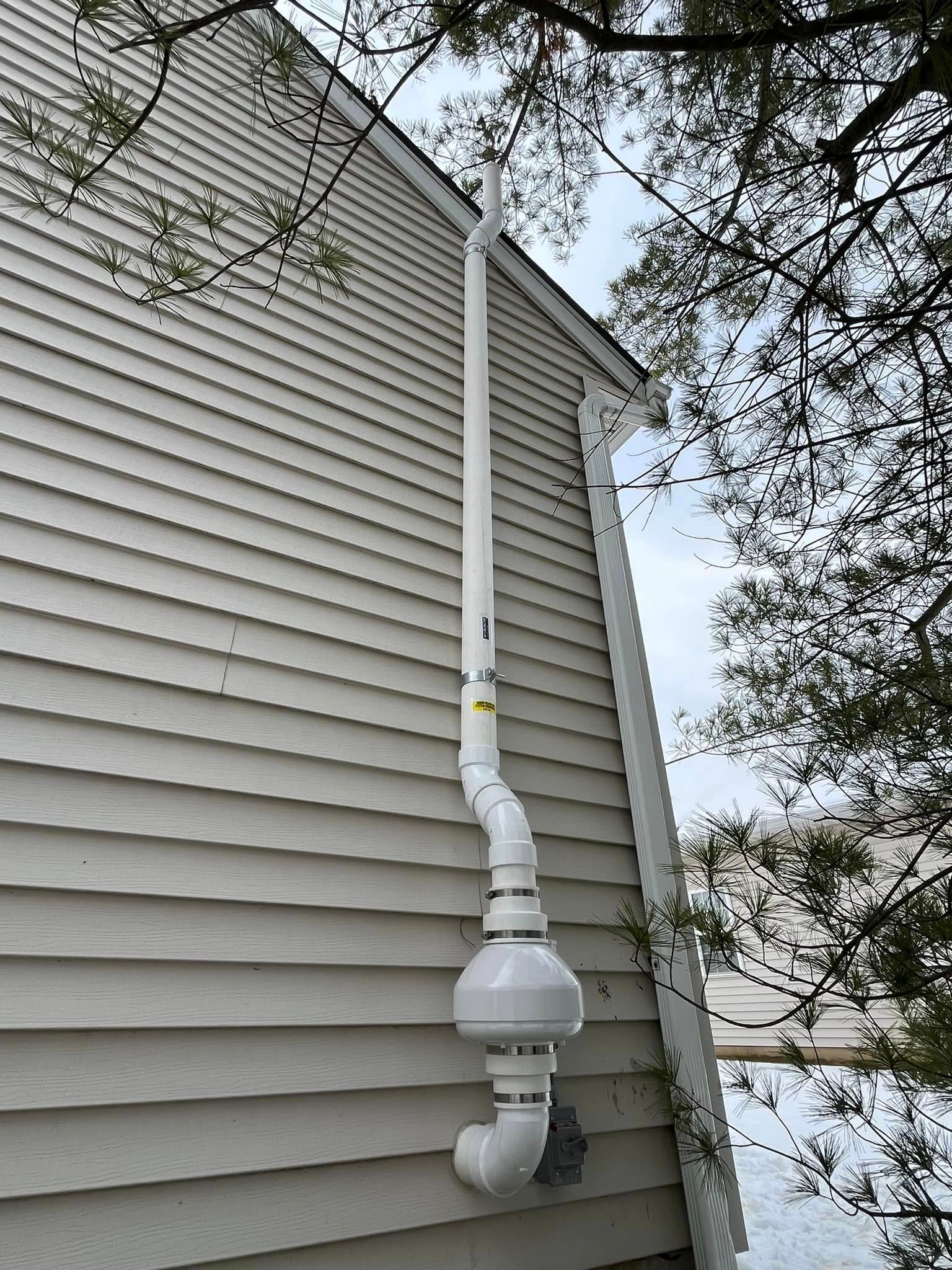A white pipe is attached to the side of a house.