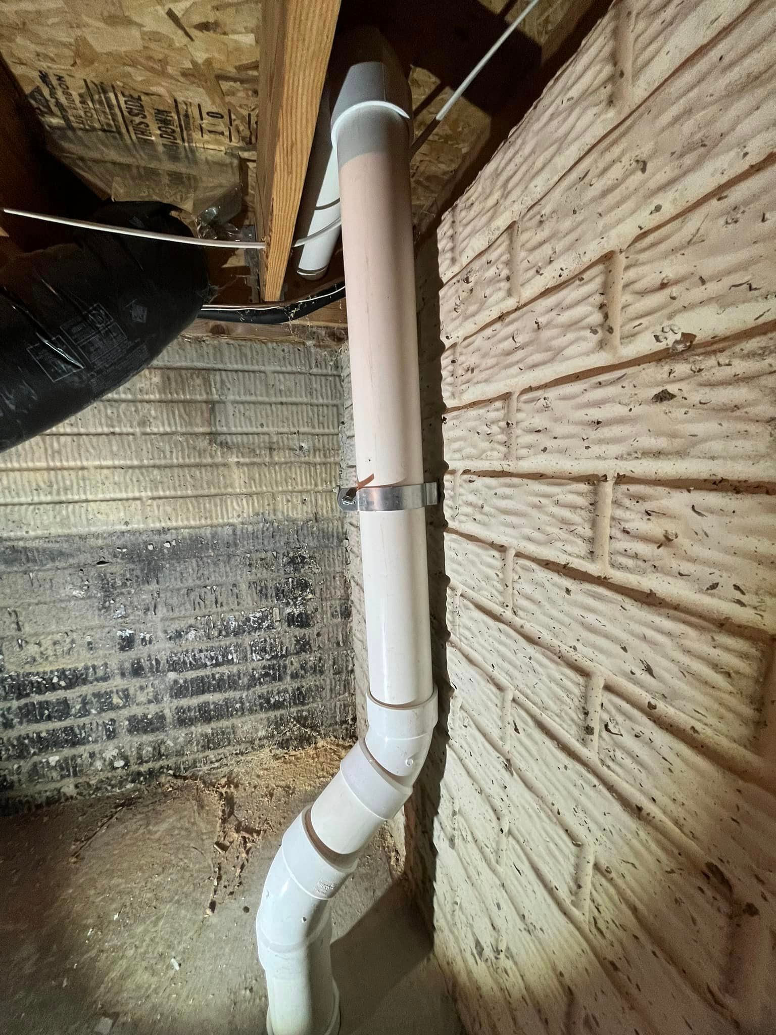 A white pipe is attached to a brick wall in a basement.