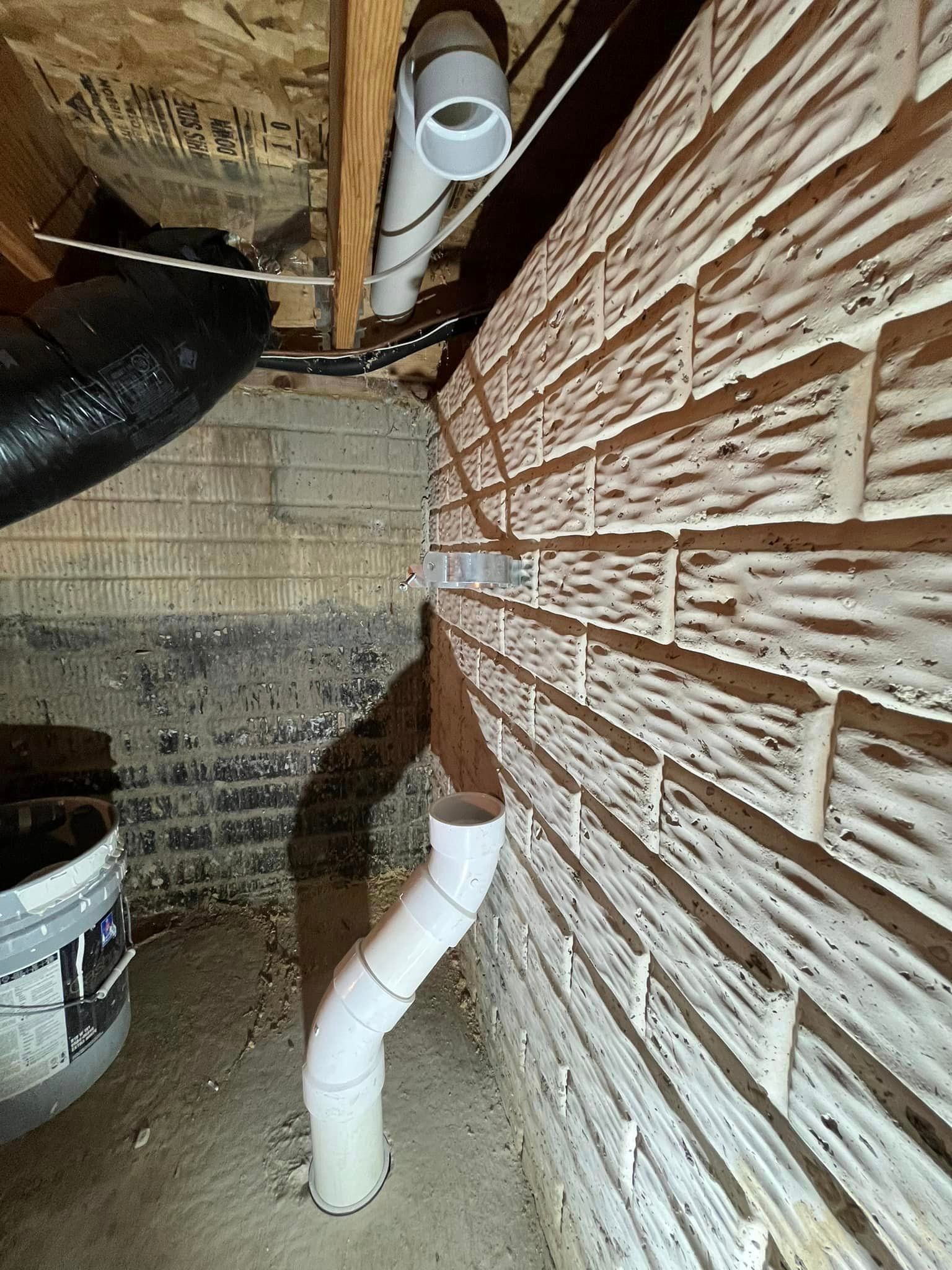 A drain pipe is coming out of a brick wall in a basement.