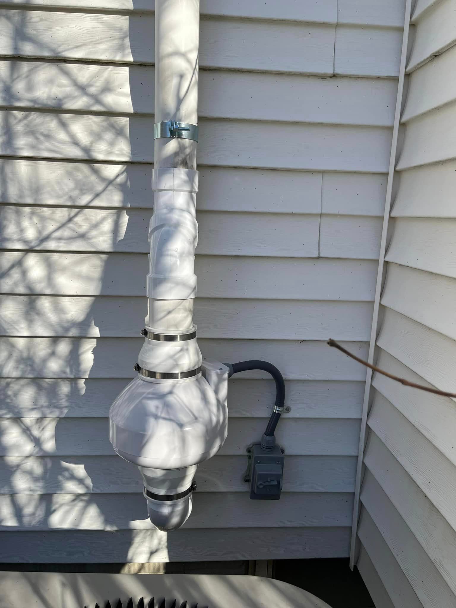 A white pipe is attached to the side of a house.