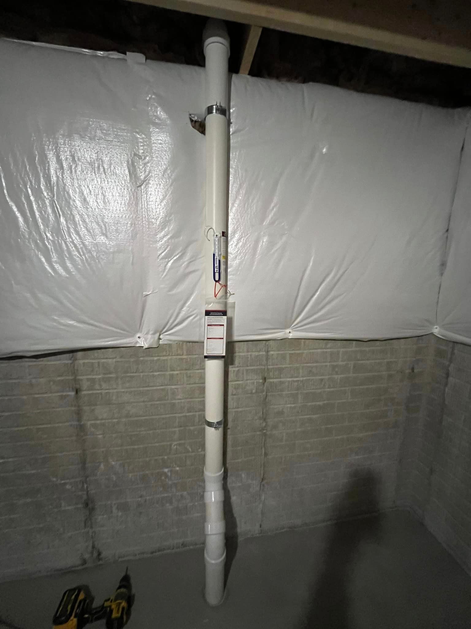 A white pipe is sitting in a basement next to a brick wall.