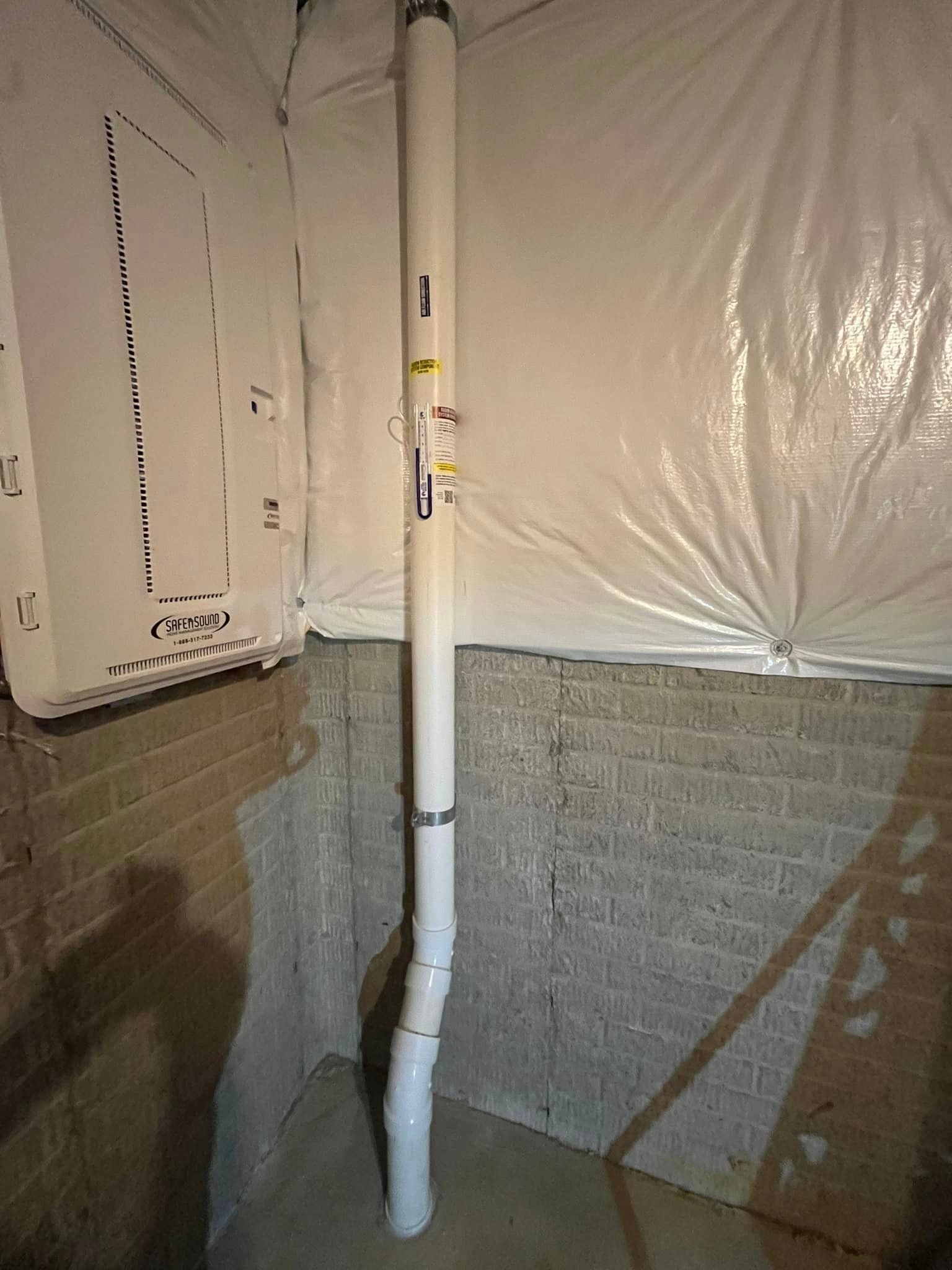 A white pipe is hanging from a brick wall in a basement.