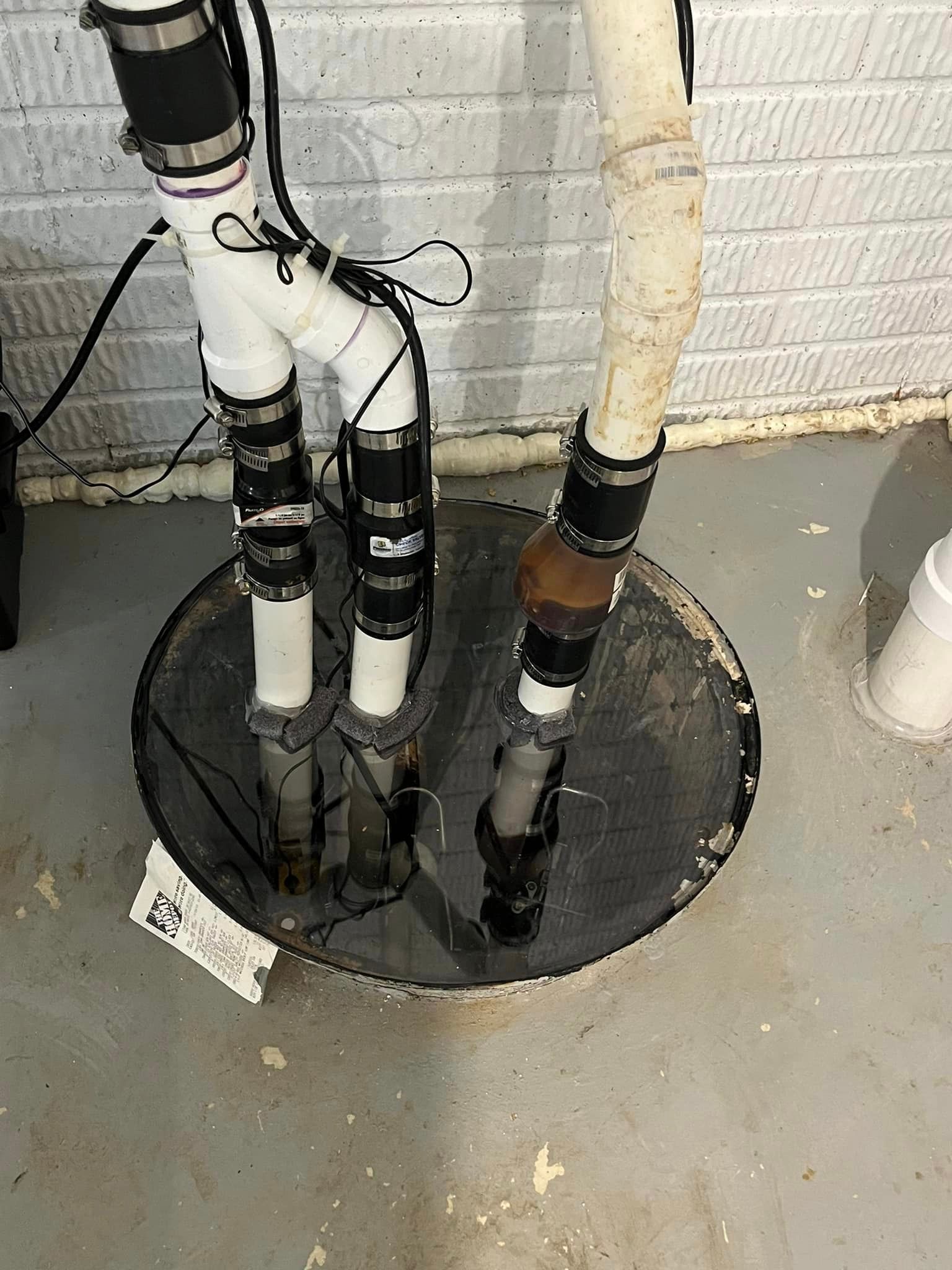 A basement drain with a lot of pipes coming out of it.