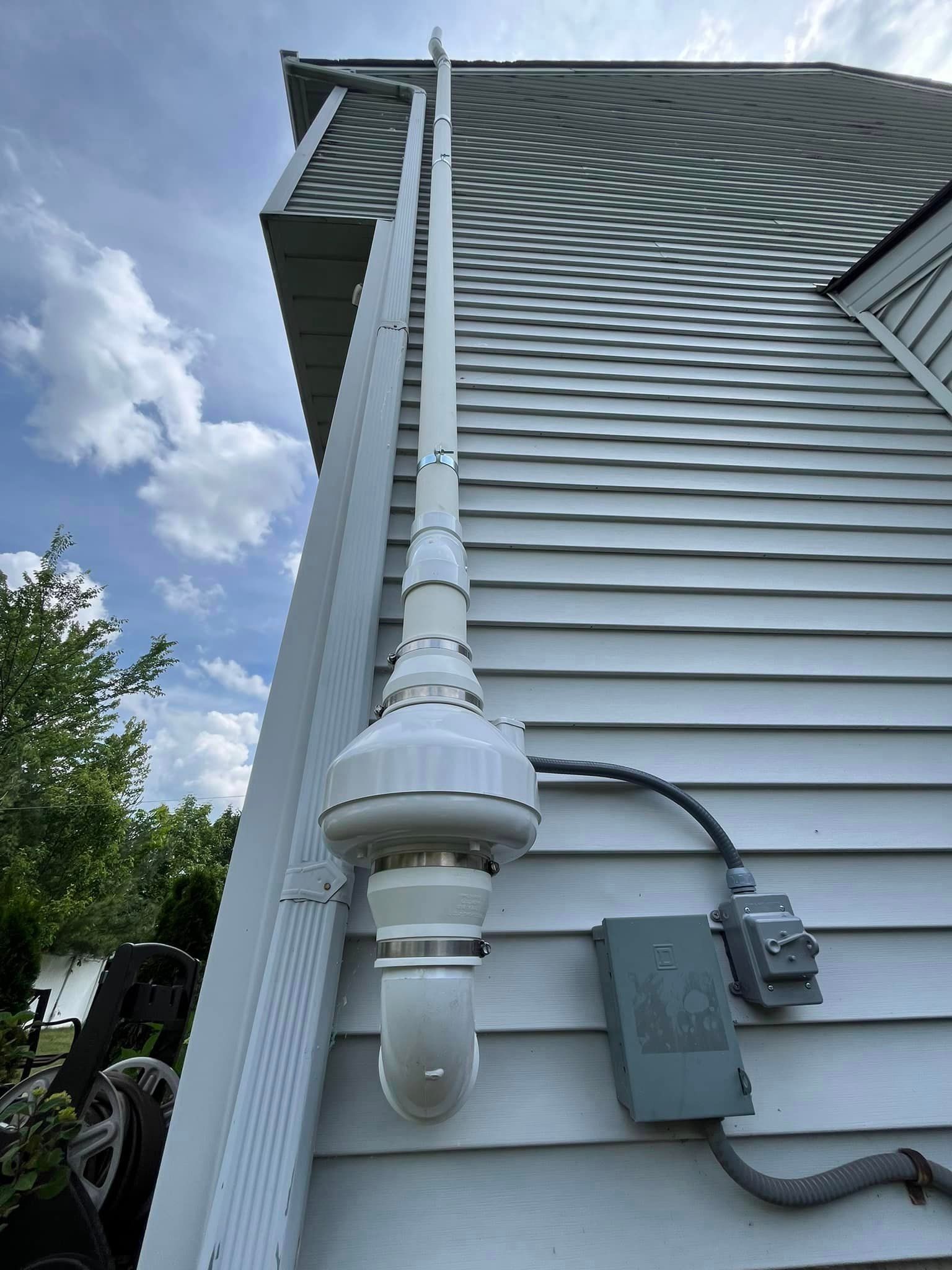 A white pipe is attached to the side of a house.