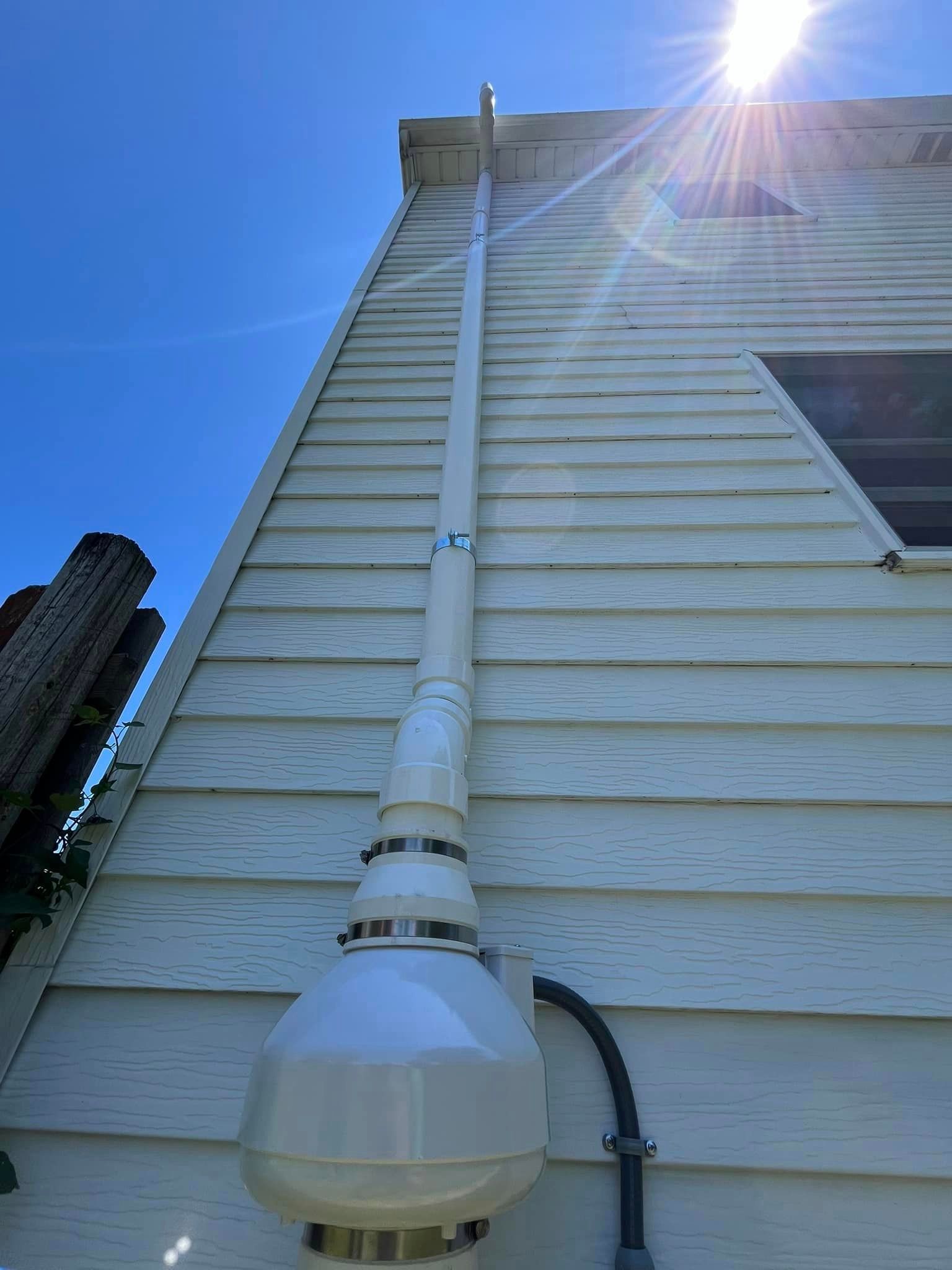 A white pipe is attached to the side of a house.