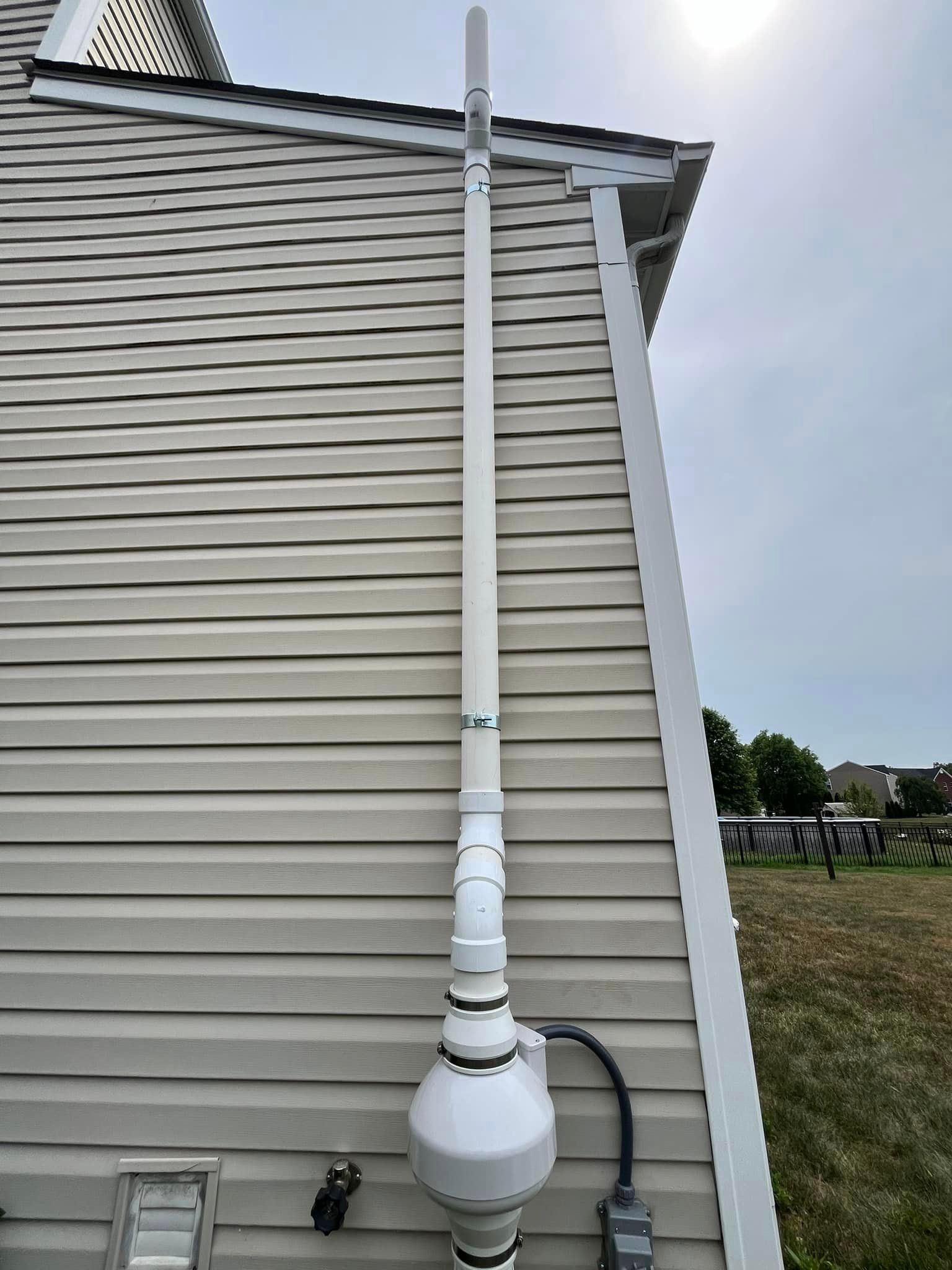 A white pipe is attached to the side of a house.
