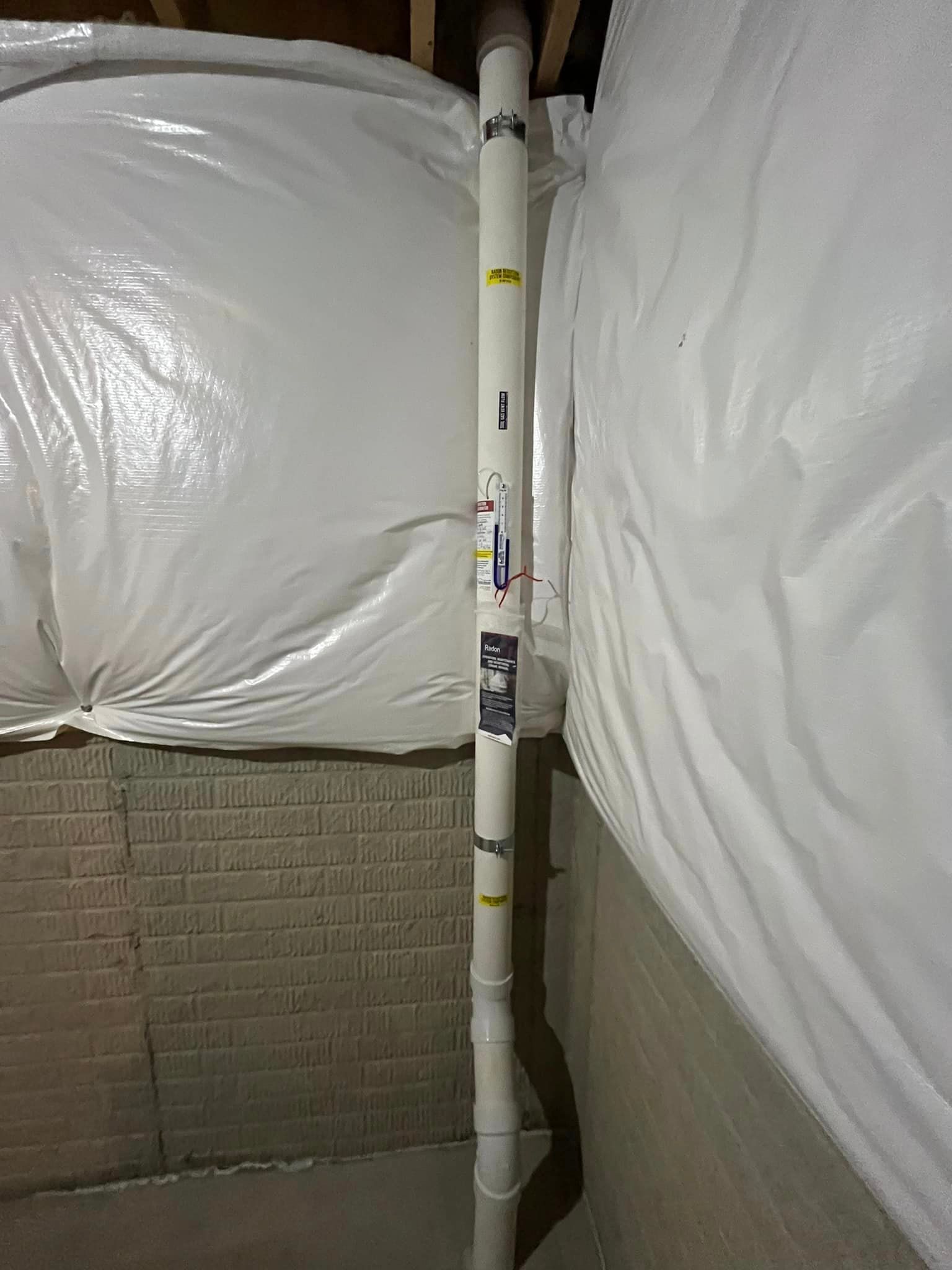 A white pipe is sitting in a basement next to a brick wall.