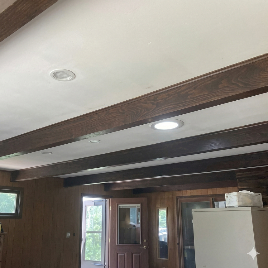 A room interior with dark wood ceiling beams, white ceiling, recessed lighting, and dark wood-paneled walls.