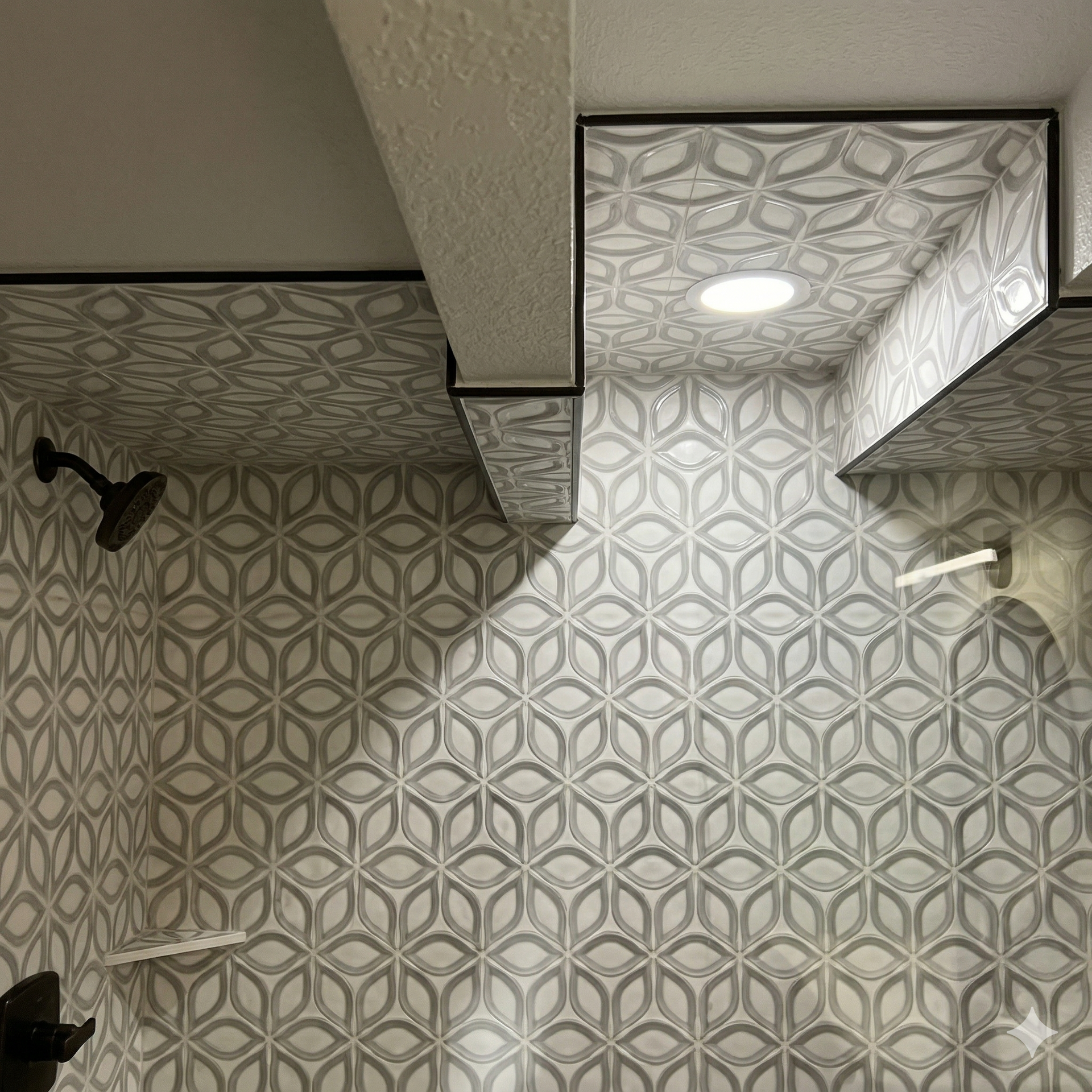 A shower stall with geometric, leaf-patterned grey and white tiles on the walls and ceiling and matte black fixtures.
