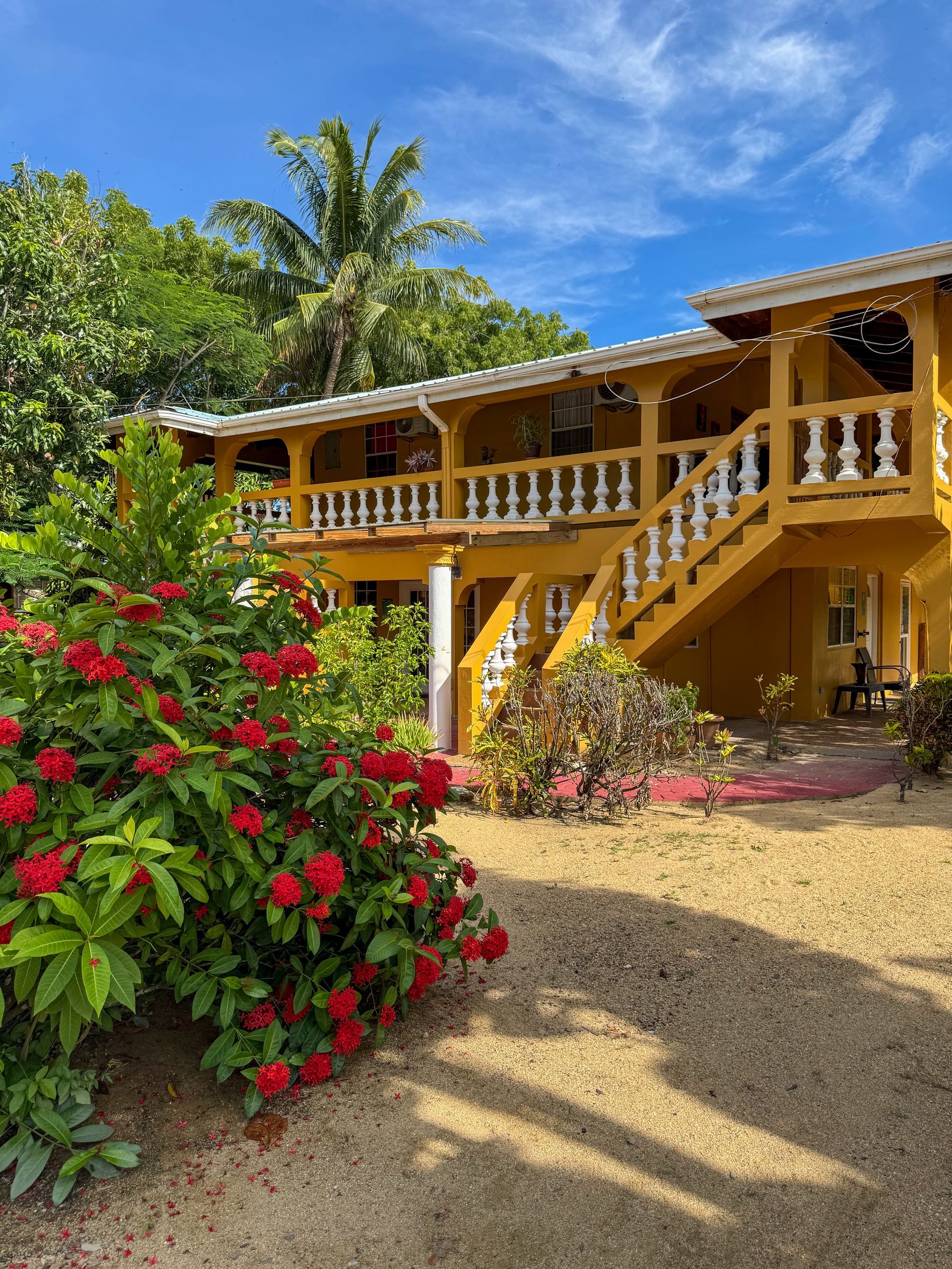 A large yellow house with stairs and flowers in front of it, Caribbean Shores B&B Building 