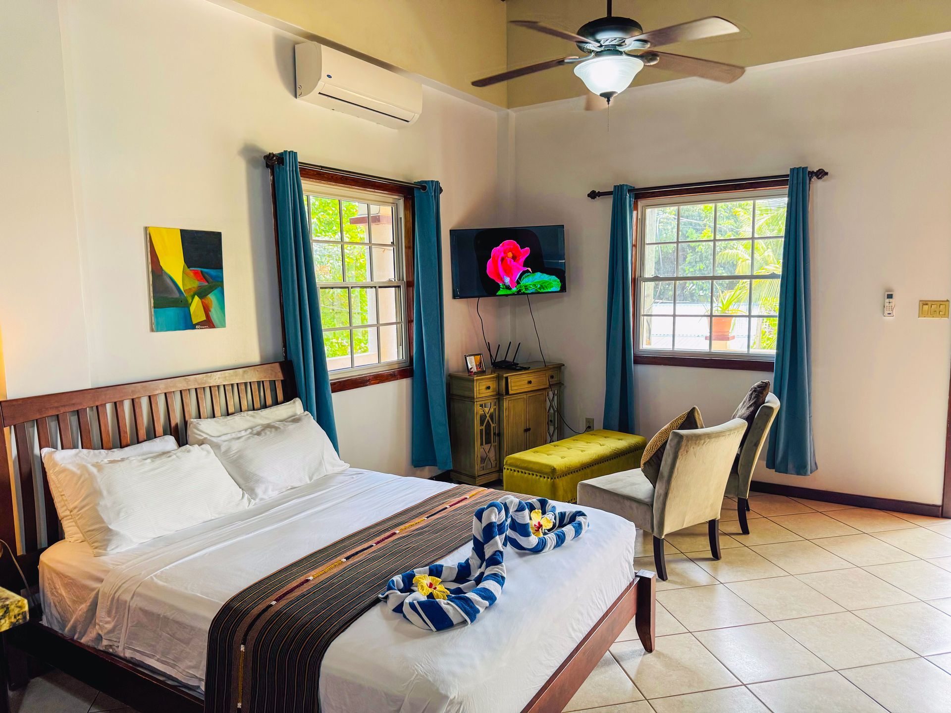 A bedroom with a bed , chairs , a television and a ceiling fan.